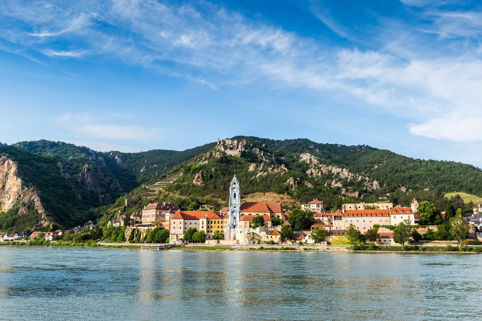 An image of a small riverside town with a hilltop castle ruin in the background