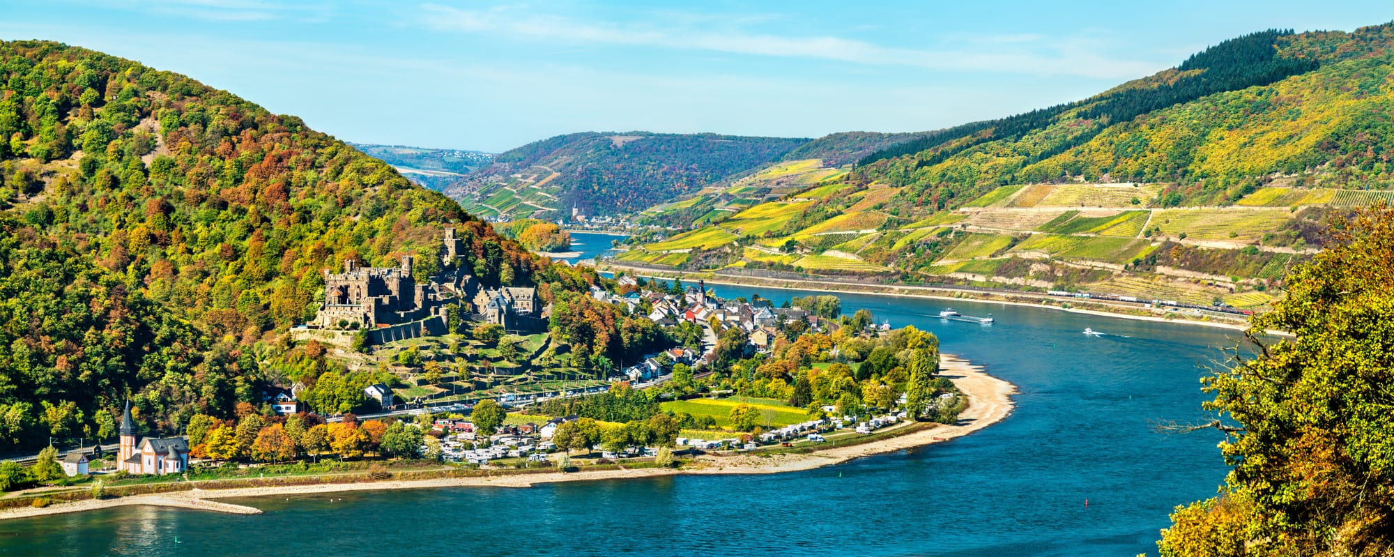 An image of a castle in the countryside on the bend of a bright blue river