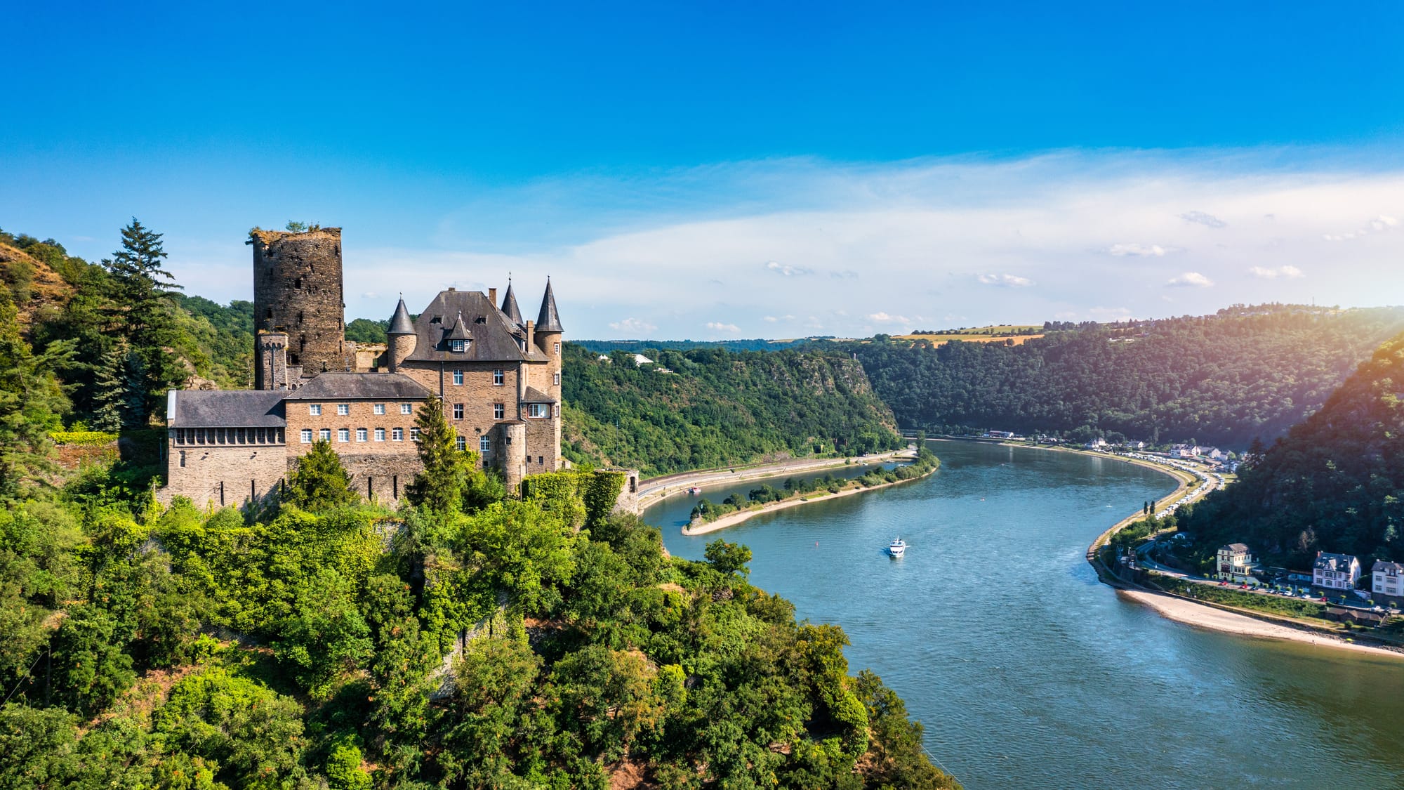 A castle overlooking a river with tree-covered steep slopes either side