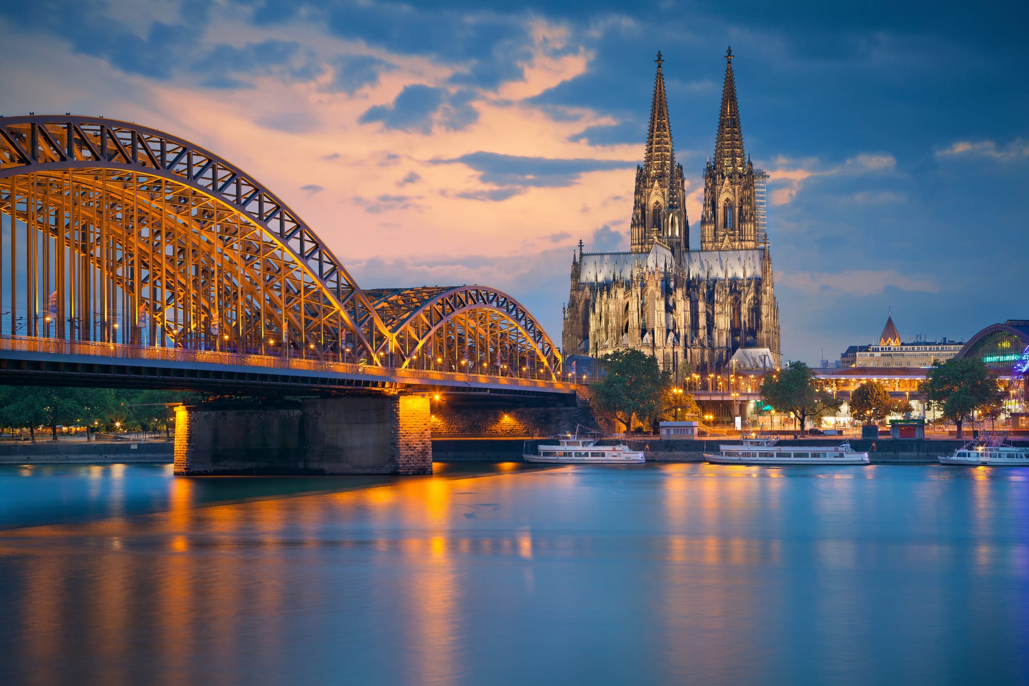 A look at Cologne Cathedral over the Rhine with an arched bridge in the foreground