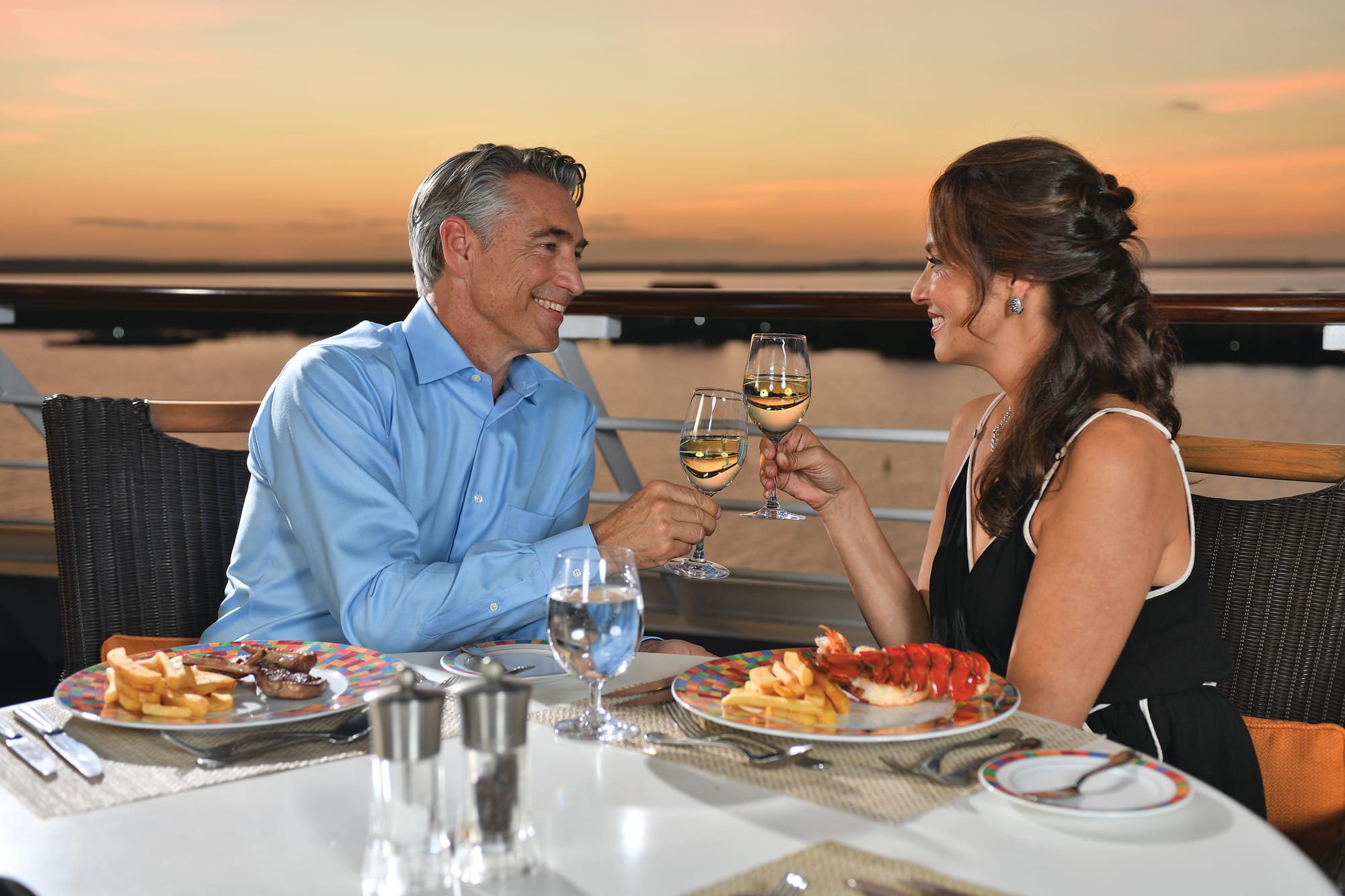 Two people sharing wine and seafood in an outside dining space on an Oceania Cruises ship