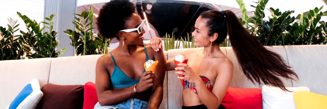Two women enjoying ice cream on a cream sofa aboard a Virgin Voyages cruise ship