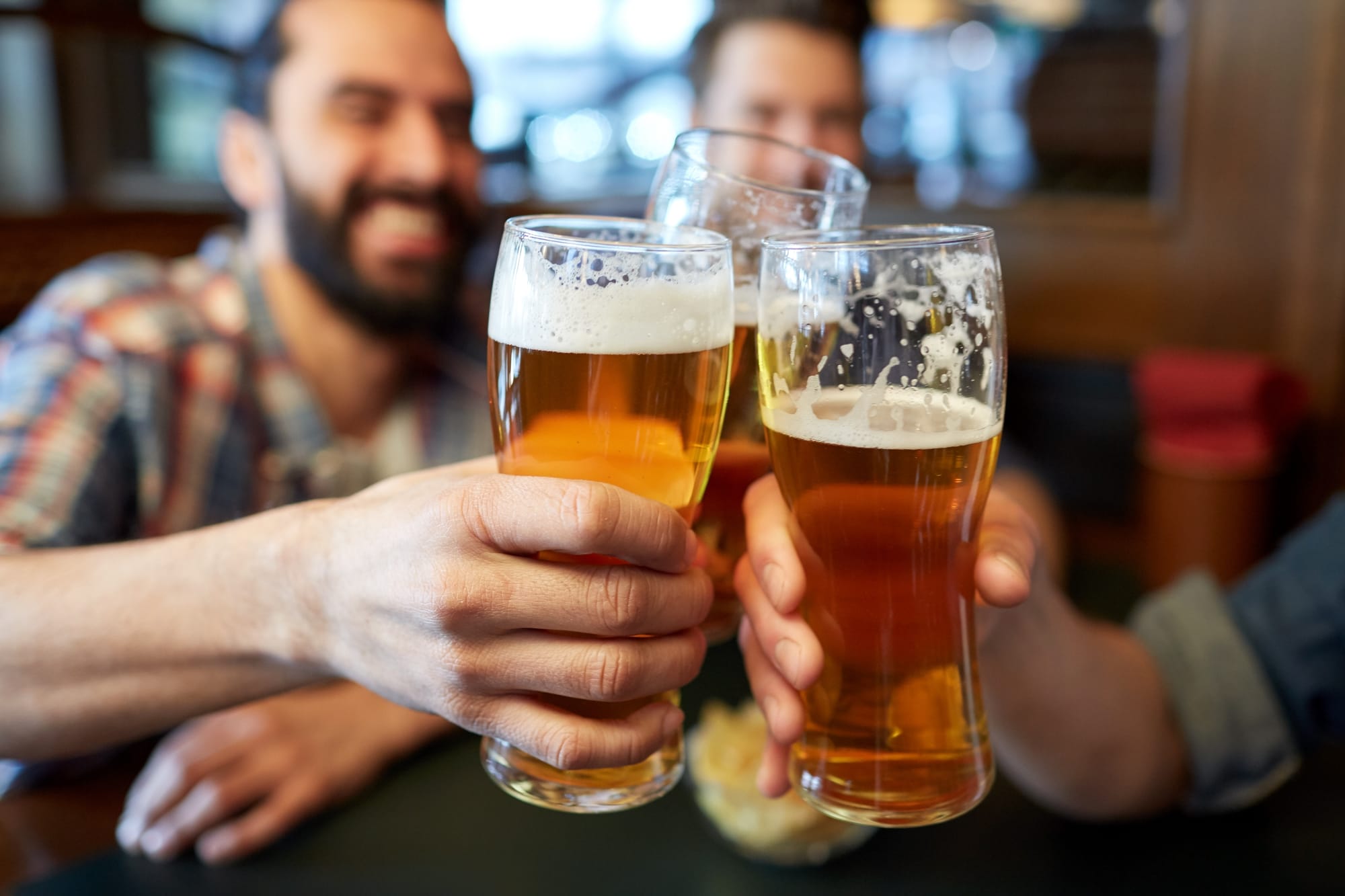 Three people drinking beers in a bar. focusing on the glasses