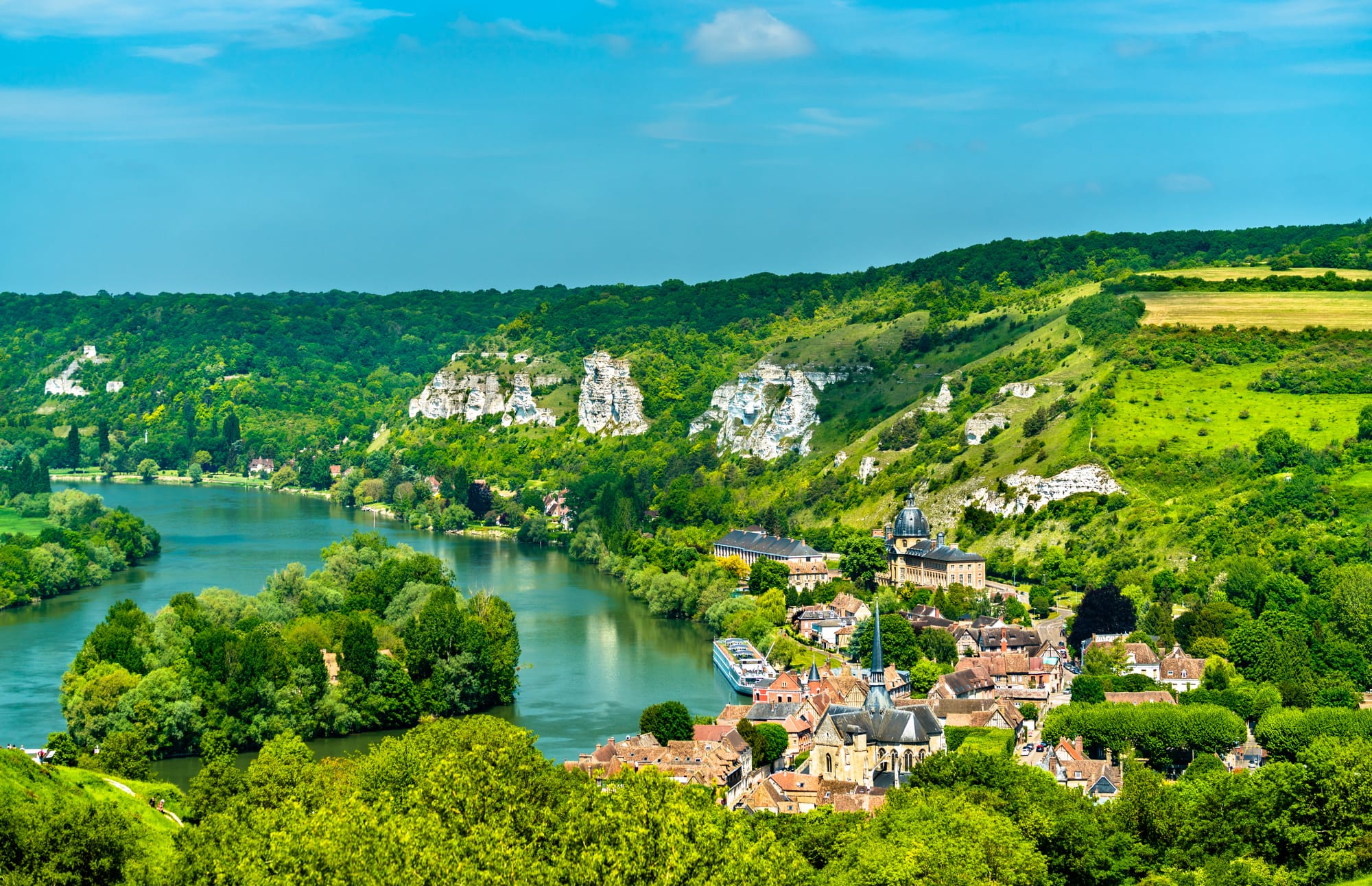 A view of the Les Andelys commune on the banks of the river Seine with green hills and forests surrounding it