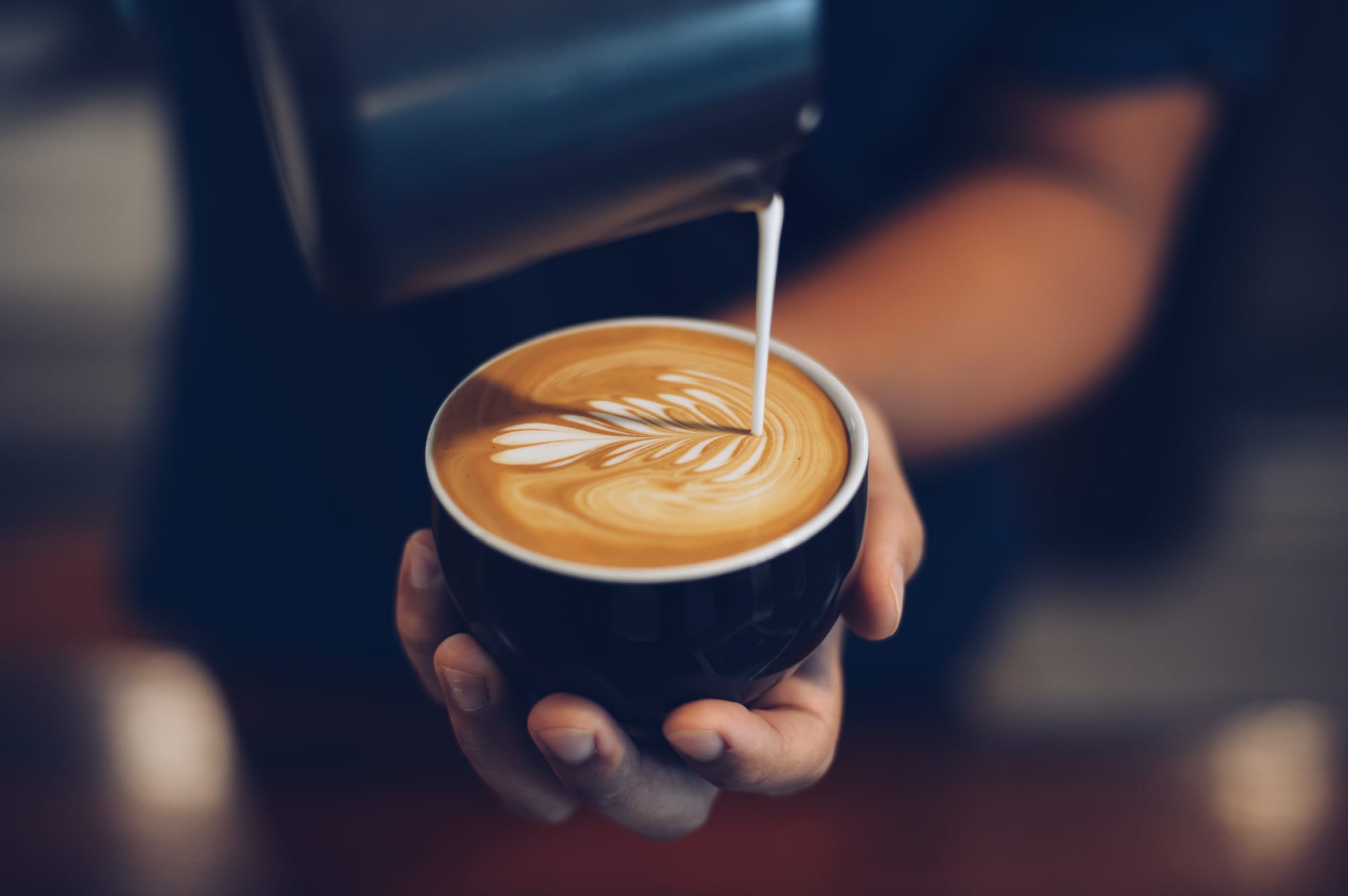 A barista pouring milk in a coffee latte