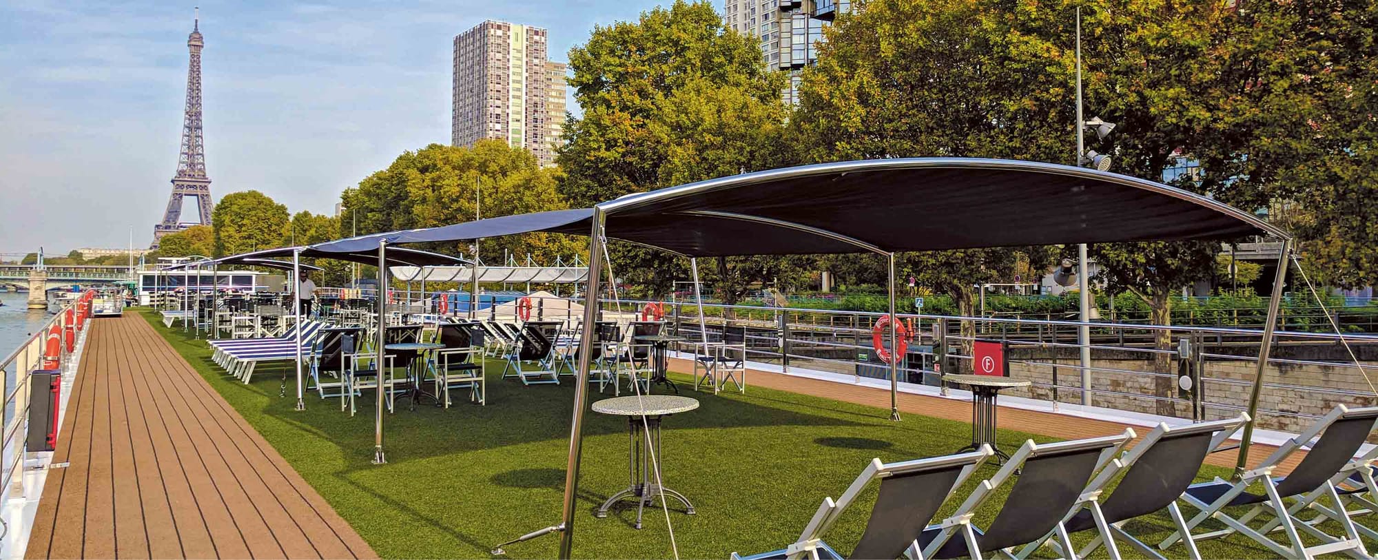 A river cruise ship sundeck with several deck chairs and a view of the Eiffel Tower in the background