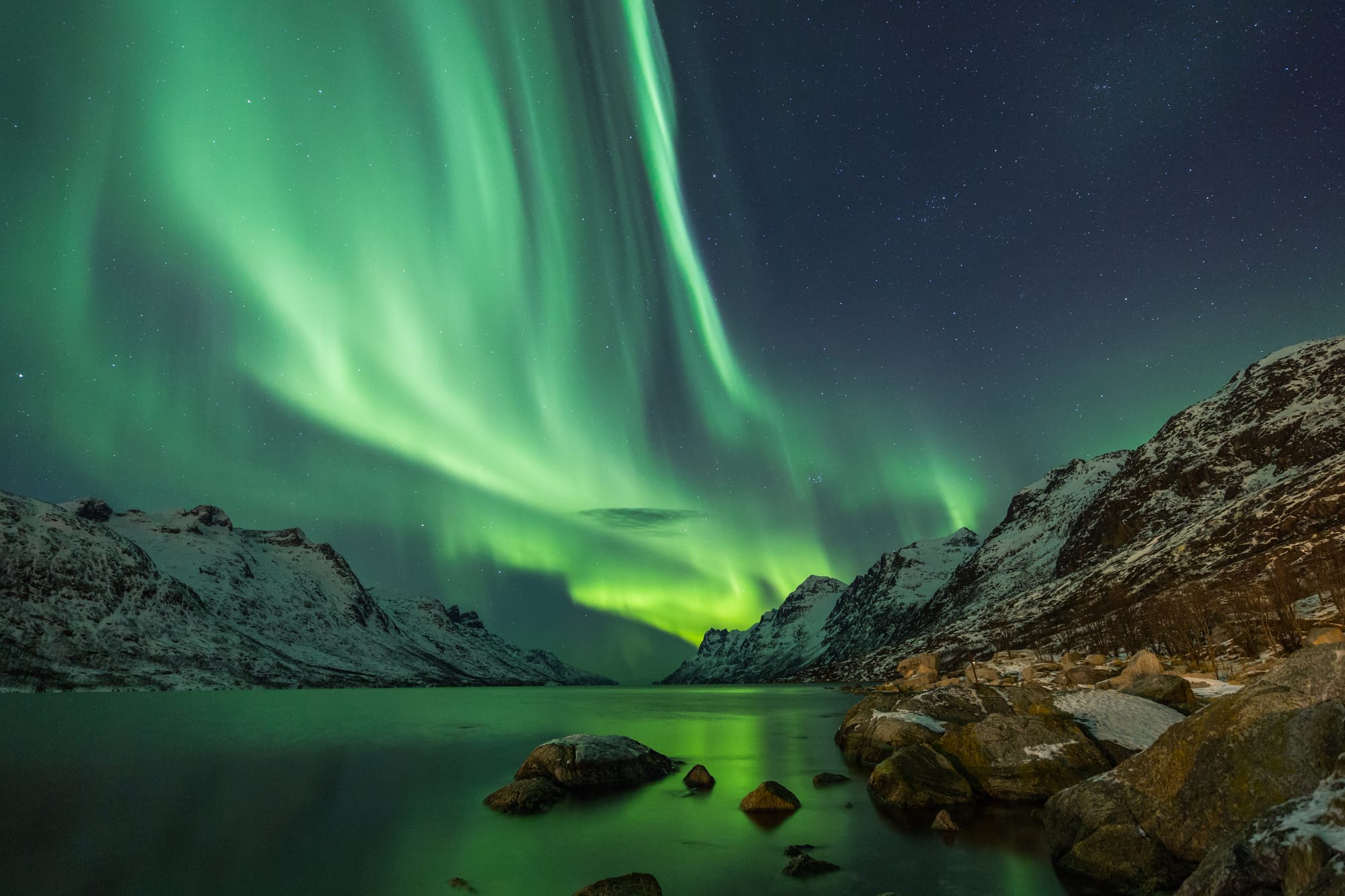 An image of the nothern lights in Norway, with green streaks of light through the night sky