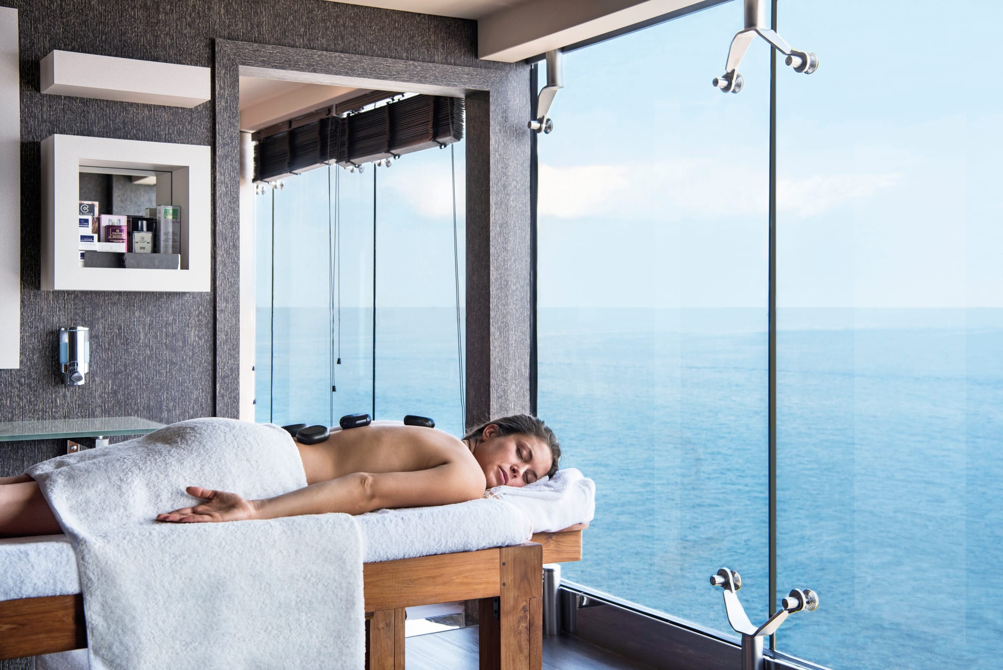 A woman lying down on a massage table in a spa with wide windows showing open ocean