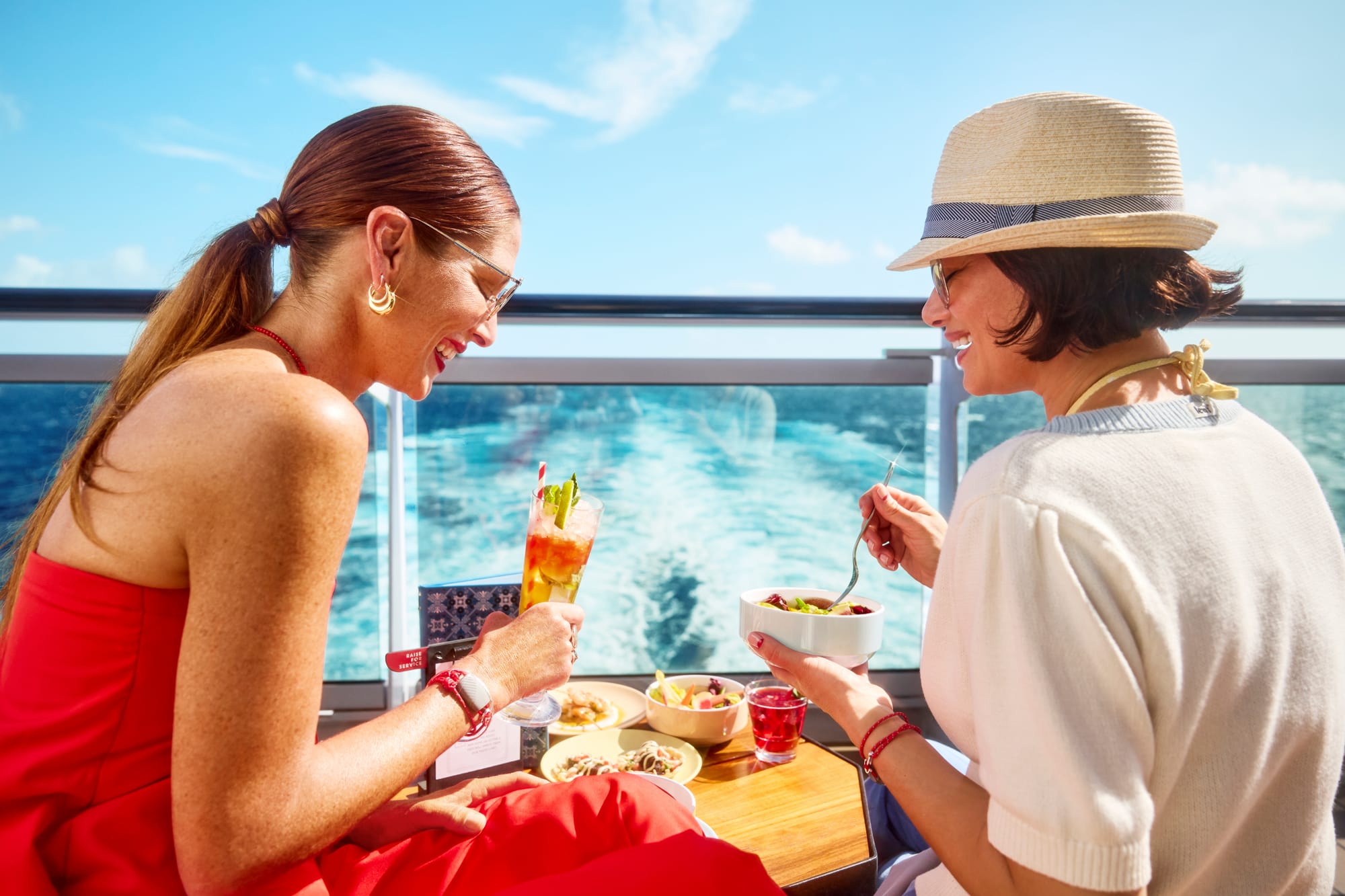 An image of a couple enjoying drinks and breakfast from a balcony, with sea views in the background