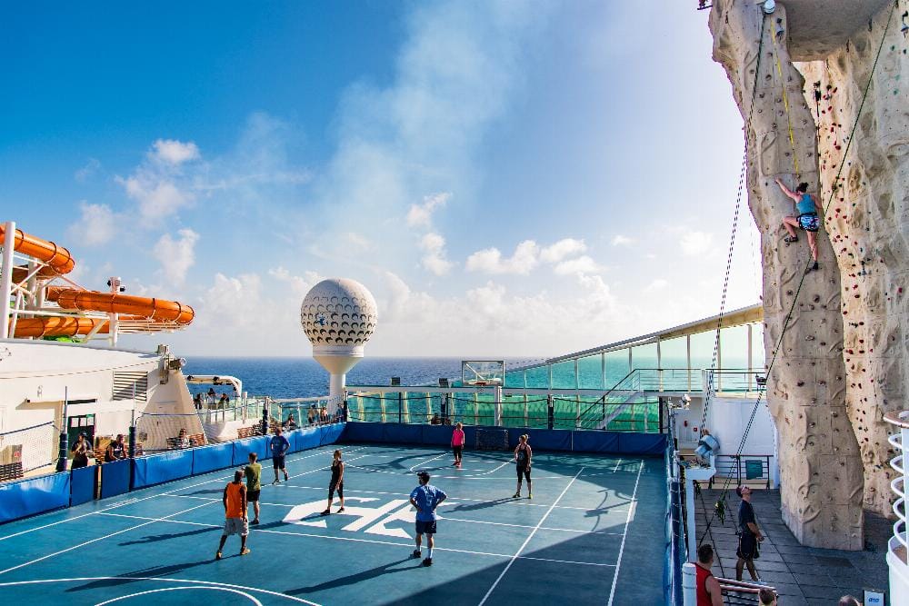 People playing on a sports court on a cruise ship with a rock climbing wall to the right