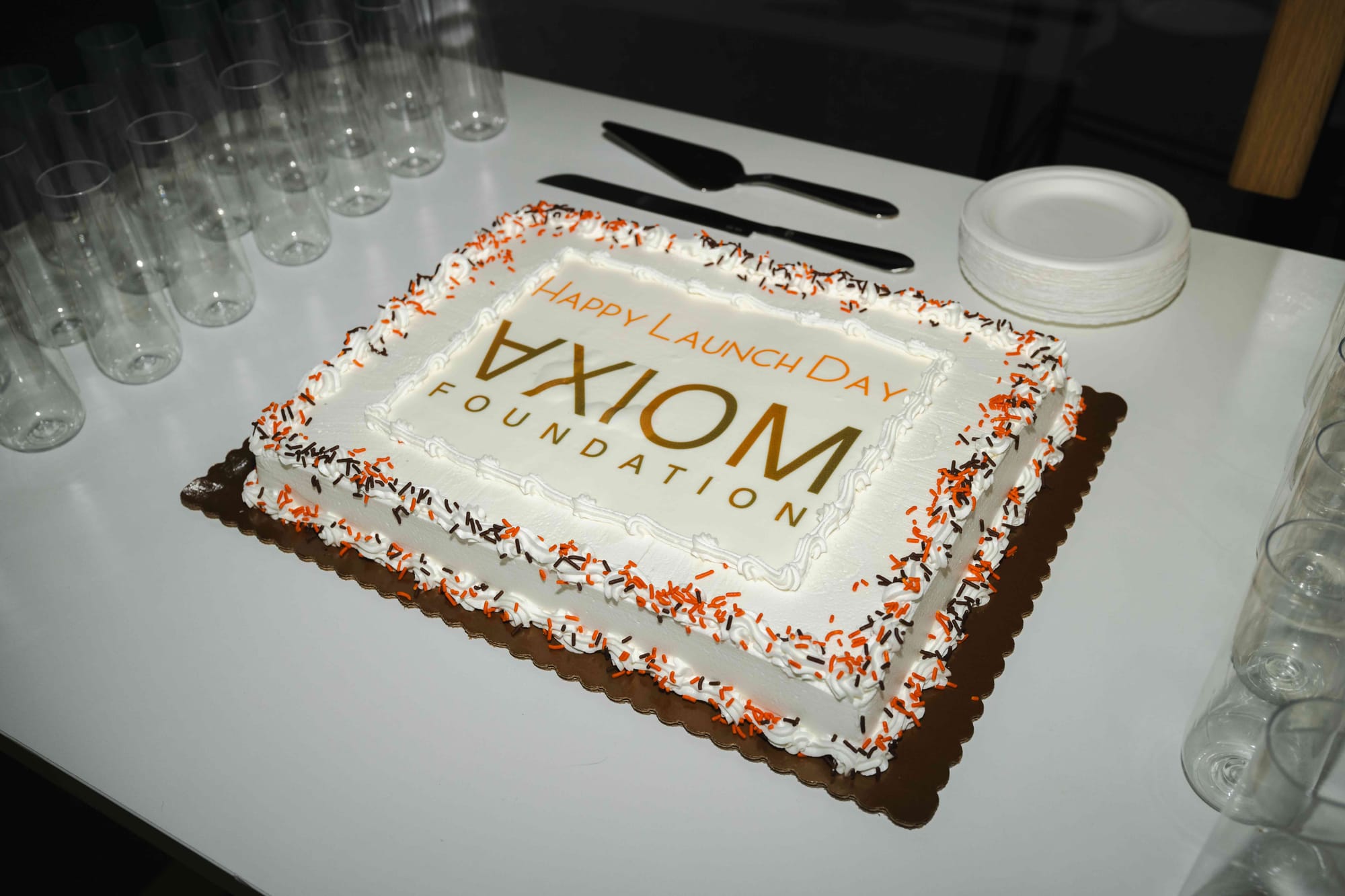 A white sheet cake with orange and brown sprinkles reading “Happy Launch Day” above the Axiom Foundation logo.