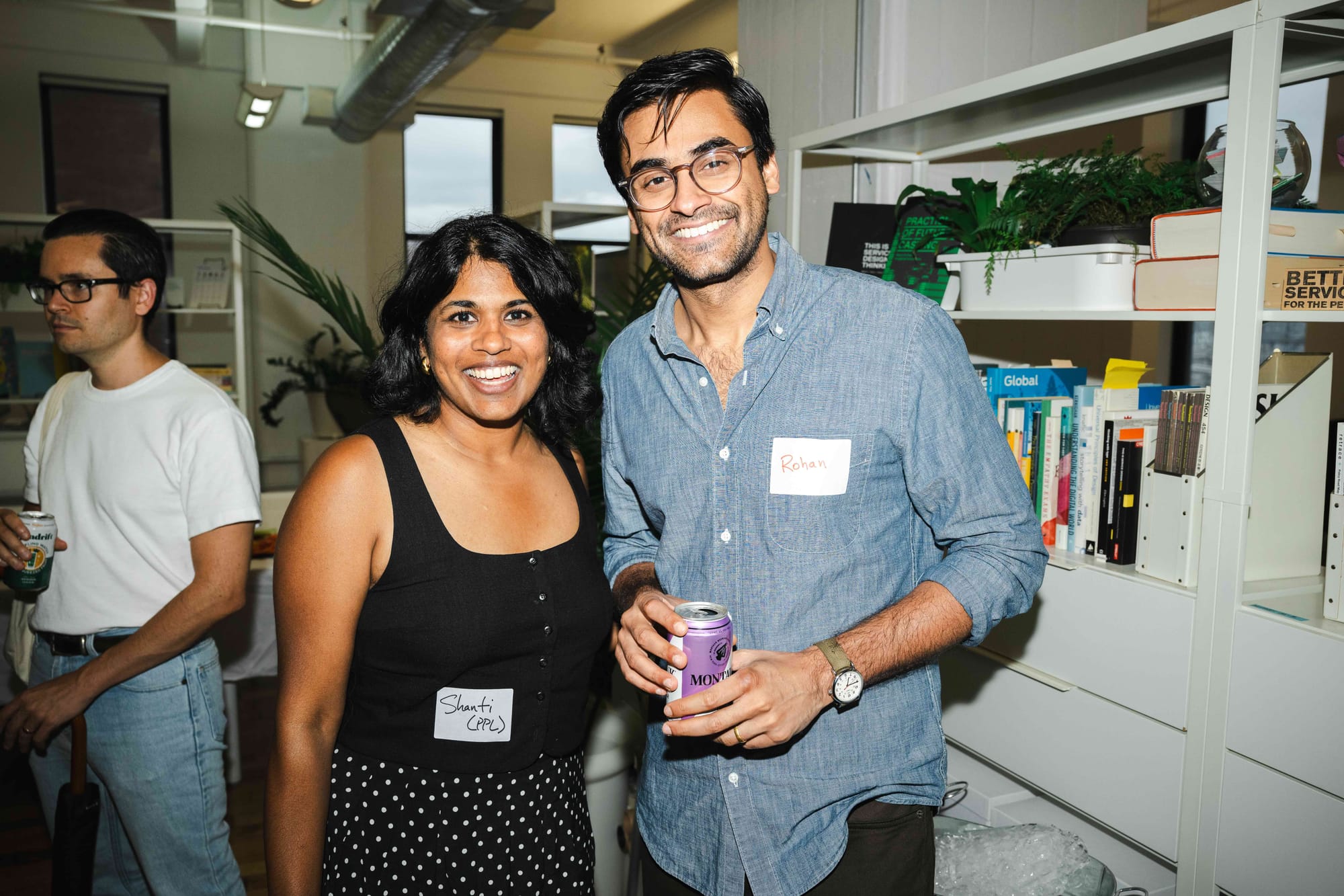Two guests smiling for the camera with drinks, in front of shelves of design and policy books.