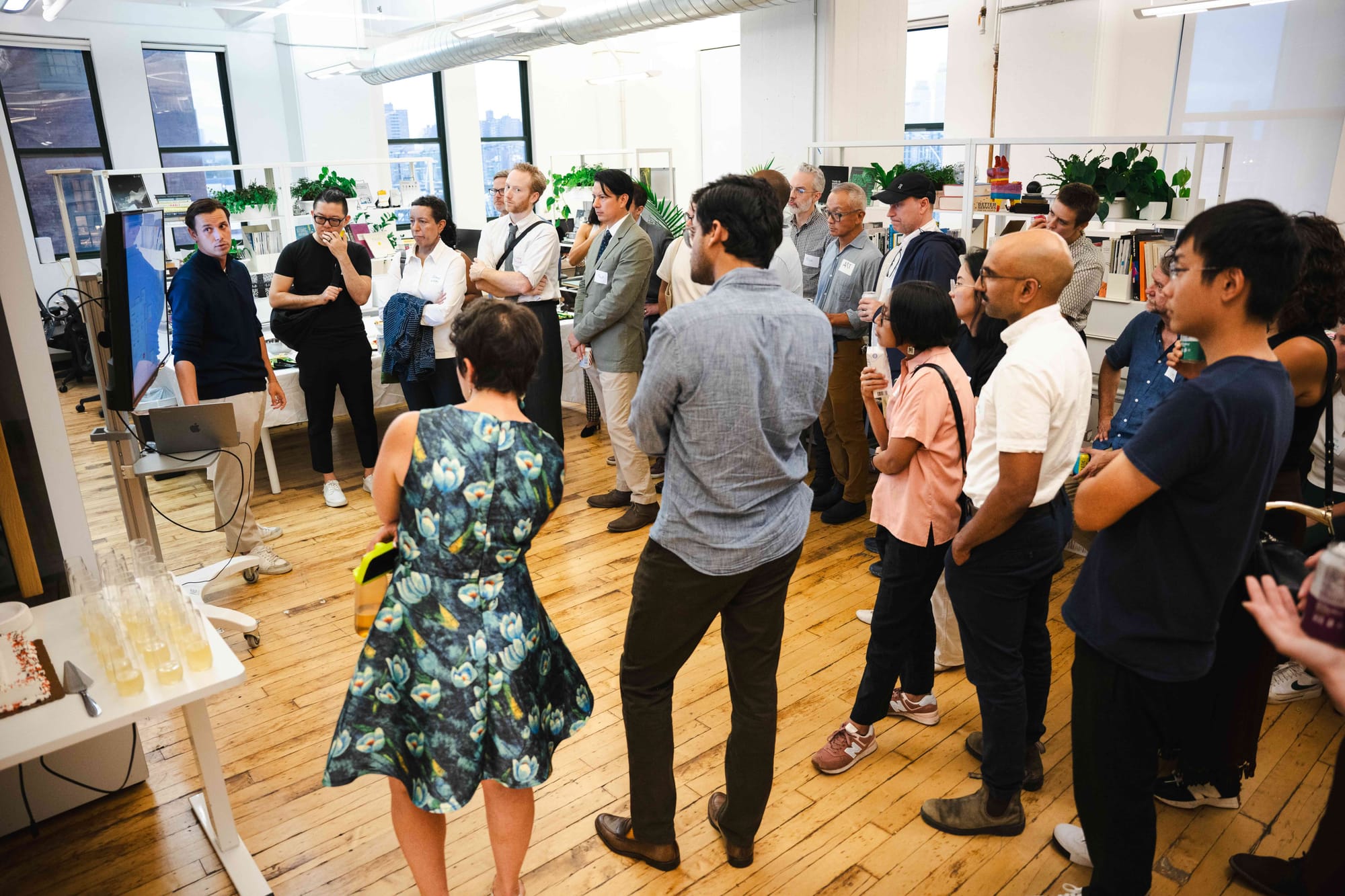 A crowd watches a live demo on a screen at the Brooklyn loft, drinks and cake on a table nearby.