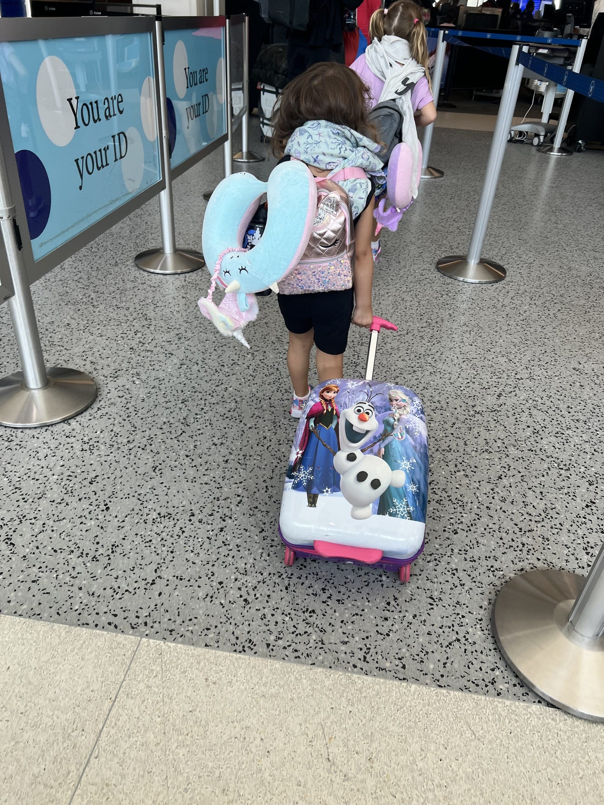 A girl pulling her own suitcase through airport security, back to camera