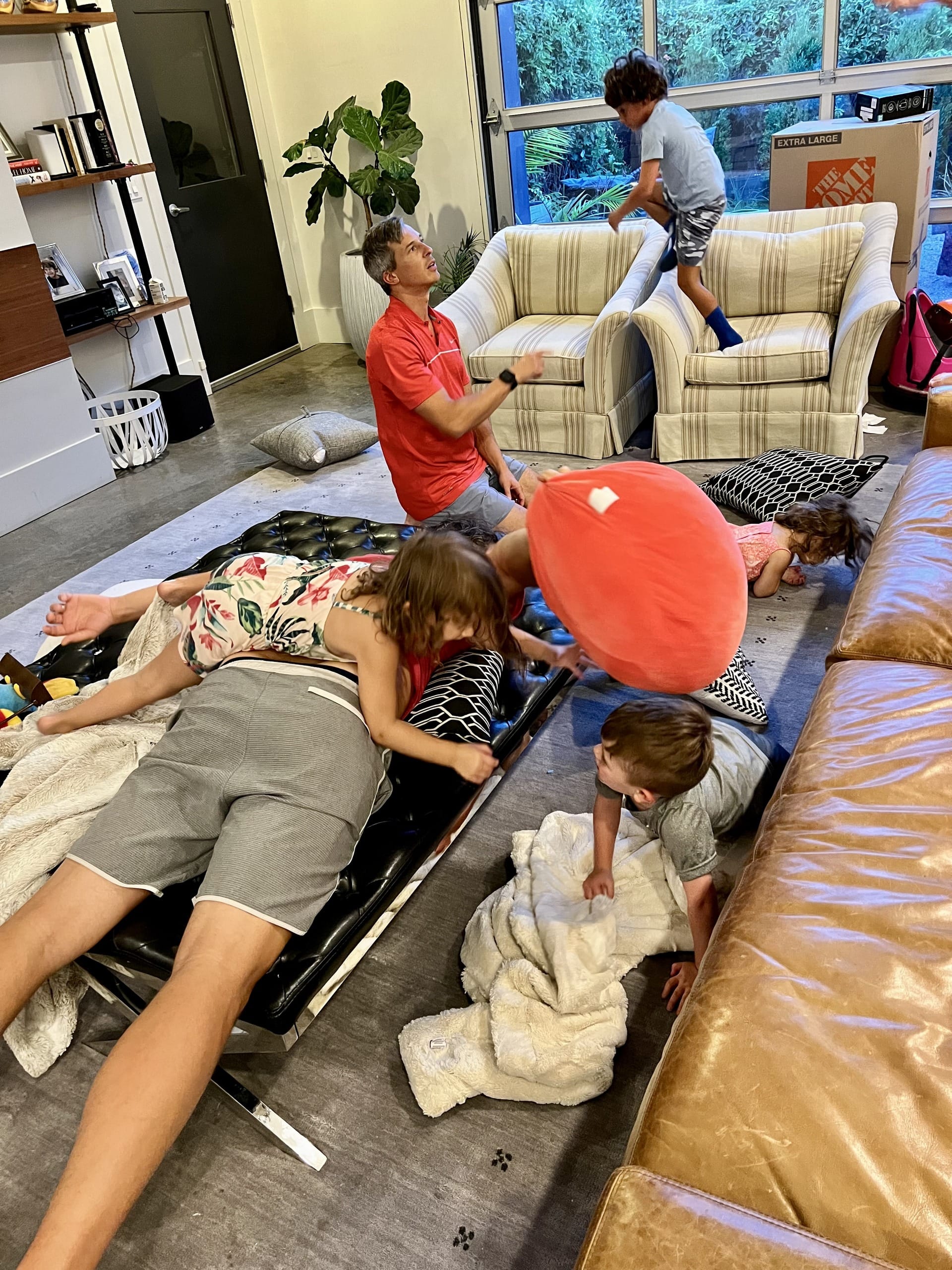 An adult and several kids play in a living room full of moving boxes during the final week before departure.