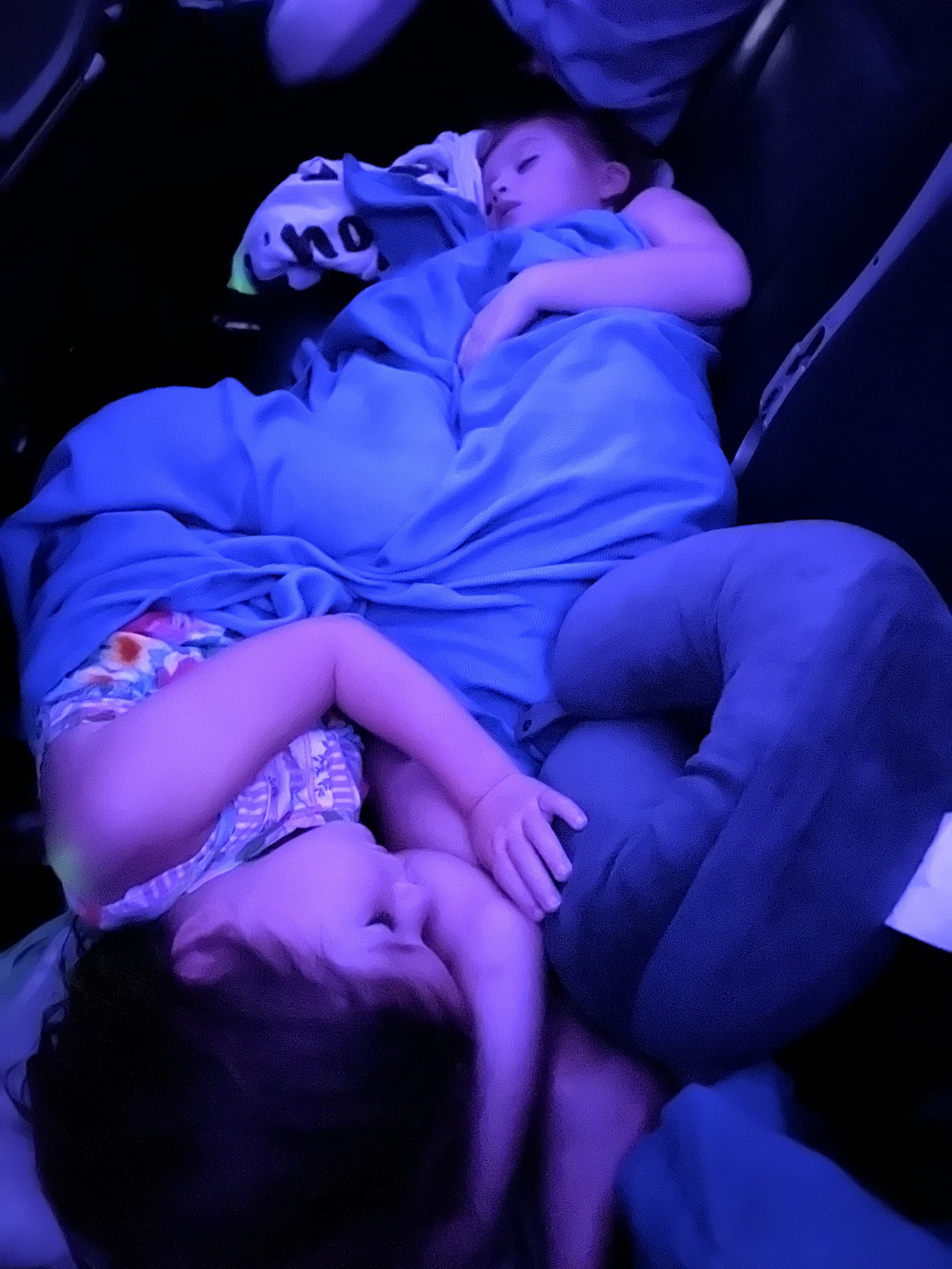 Two girls asleep across a lap during the overnight flight, dim cabin light
