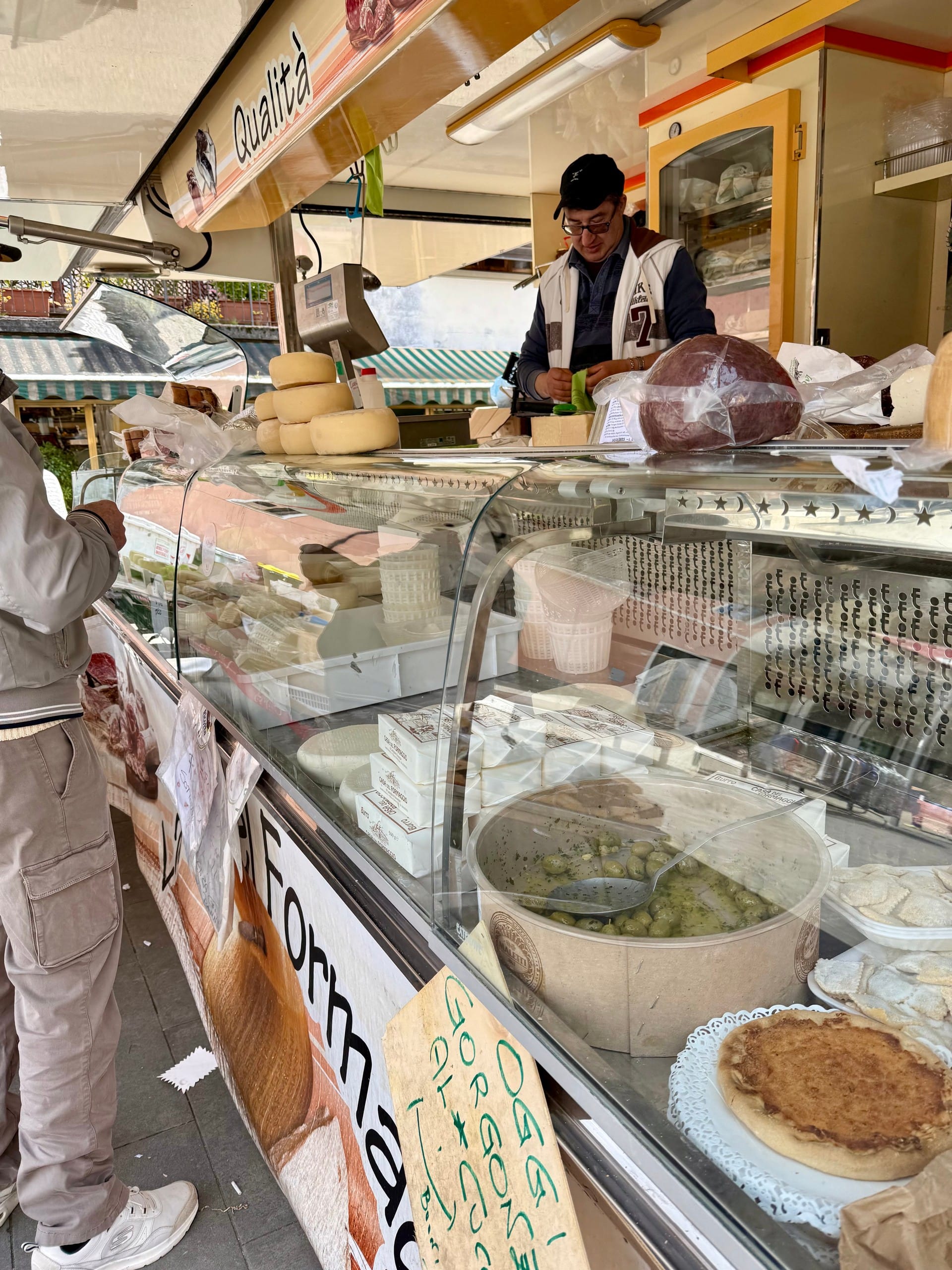 Wheels of pecorino cheese stacked beside a scale at a market stall in Barga, Italy