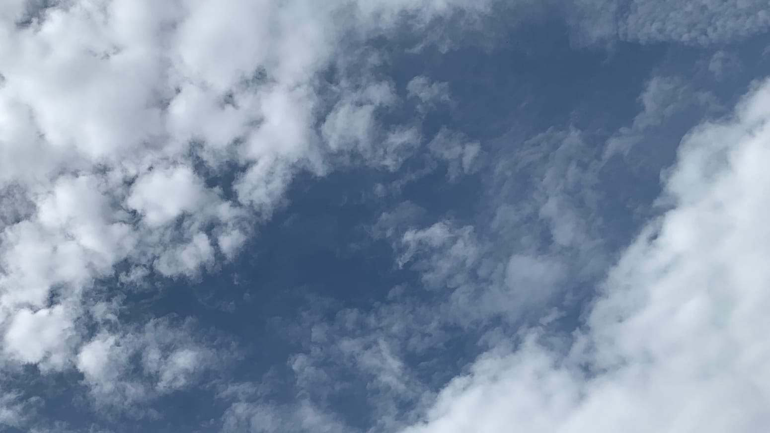 A deep, desaturated-blue sky with fuzzy clouds on each side I don't know the Science names for these sorry the just look kind of like cotton that has been pulled at and is all scraggly