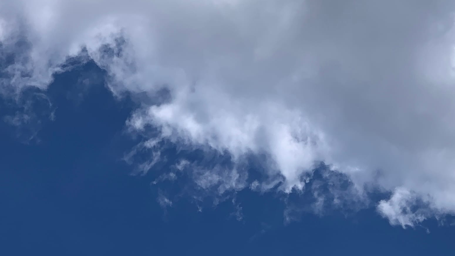 A frame divided roughly diagonally between deep blue sky in the lower left corner and gray-white cloud in the upper right, with a bright patch of cloud in the center where they meet, which is trailing white tendrils