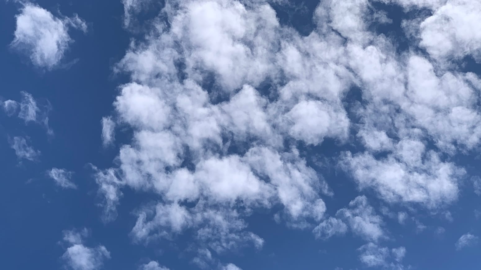 Deep blue sky partly covered with clustered little puffs of cloud leave deep blue gaps between them.