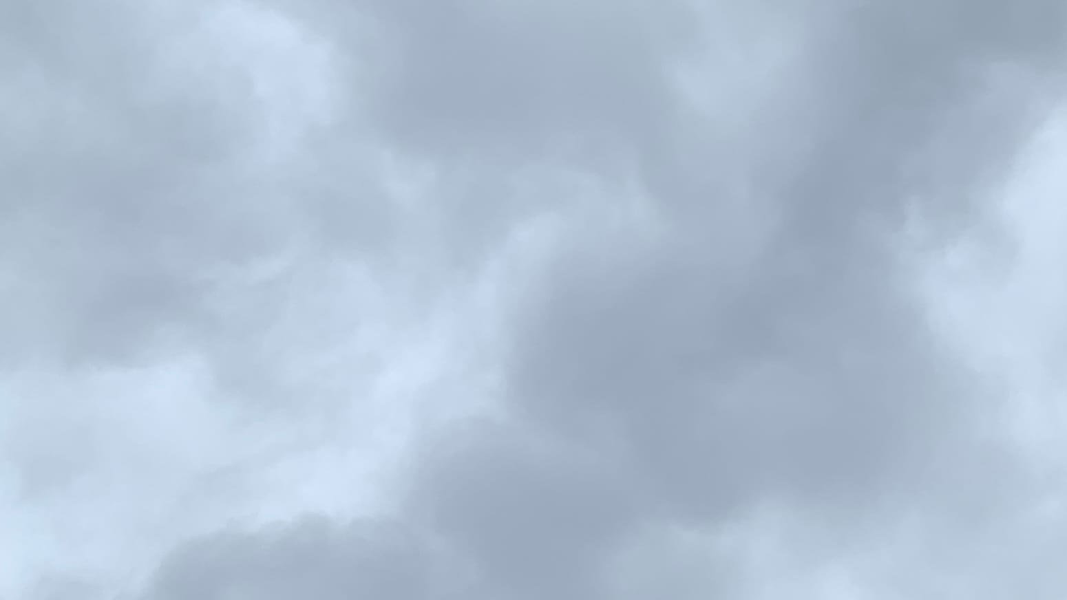 A patch of sky covered in clouds in various shades of gray. An arm of paler gray, twisting back and forth as it tapers to a pont, reaches up from the bottom left corner, running roughly parallel to a lumpy band of darker gray. 