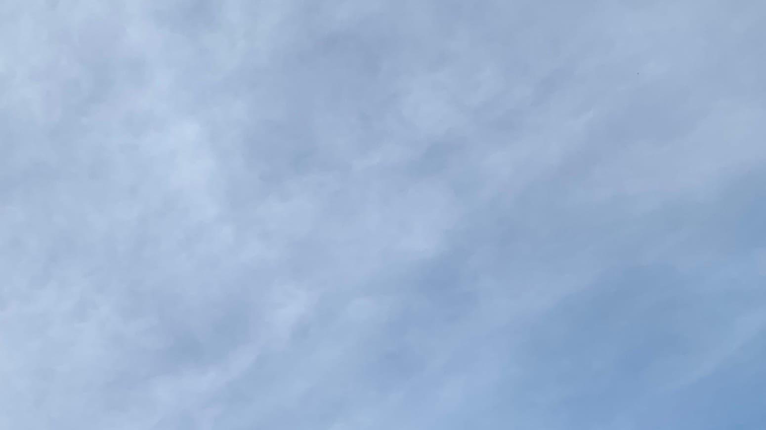 A patch of sky in blurrily mottled white and blue, with more white toward the left and more blue to the right, and with an indistinct grain running diagonally from lower left to upper right.