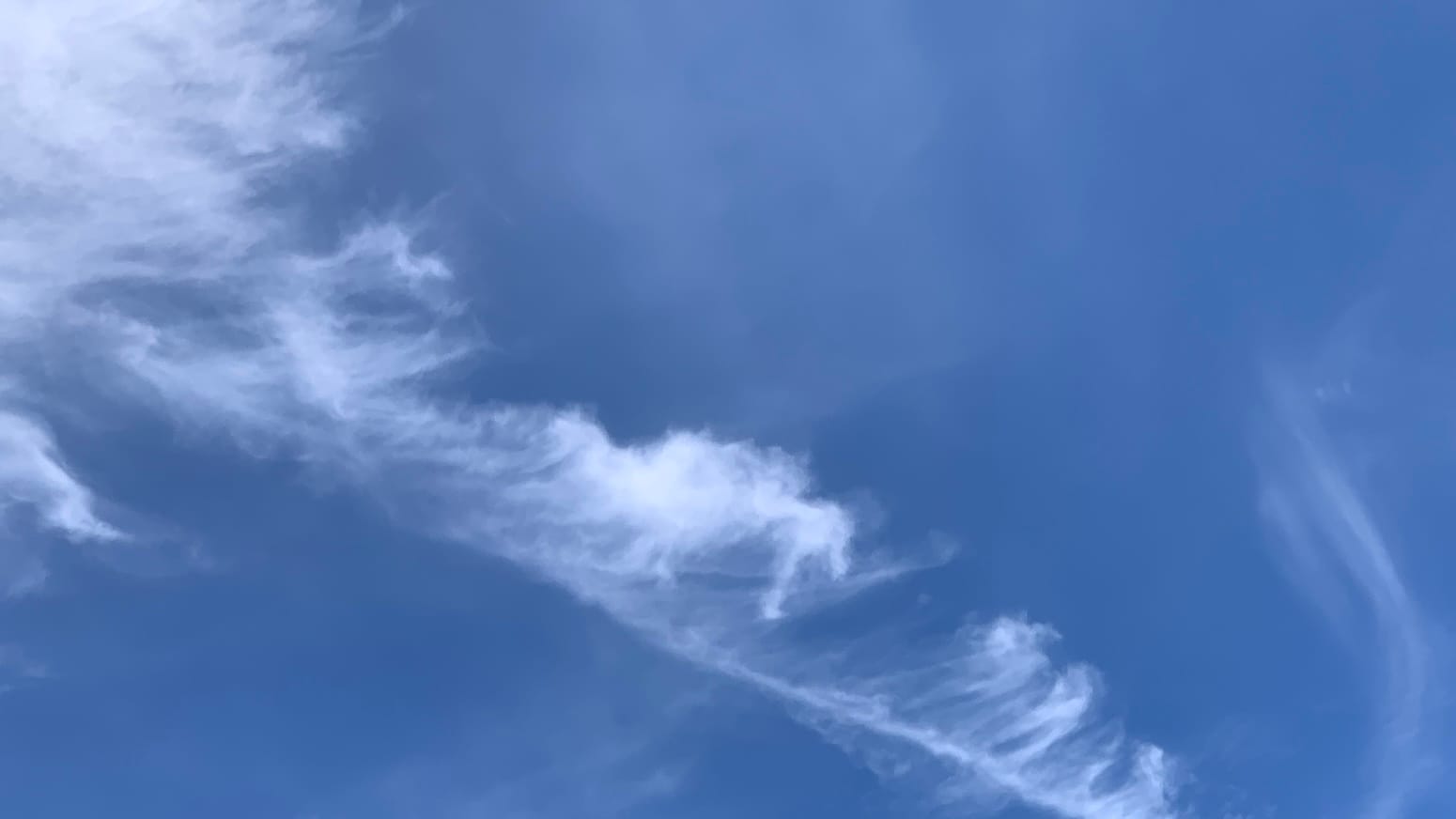 Blue sky with swirls of transparent white on it and a sort of feathery white cloud formation extending diagonally down from the upper left corner, and a curving double-wisp at lower right.
