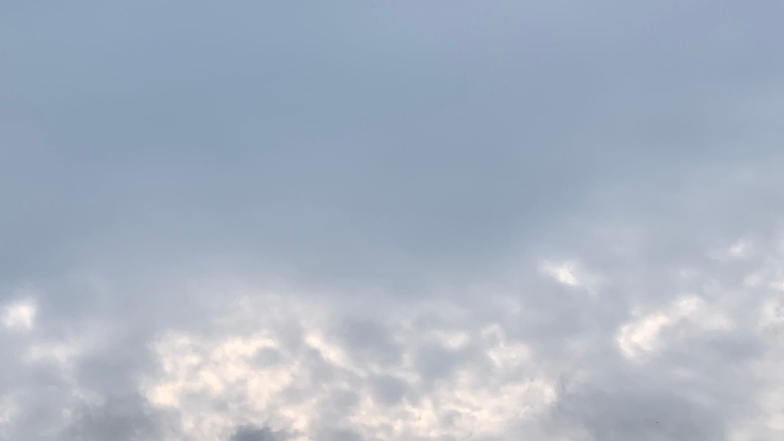 A patch of gray sky that turns mottled with brighter, whiter bits at the bottom of the frame. 