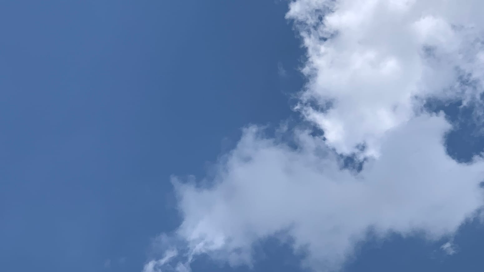 Blue sky with a white cloud in the upper right corner and an oddly depthless gray cloud overlapping the bottom of the white cloud, taking up most of the lower right quadrant.