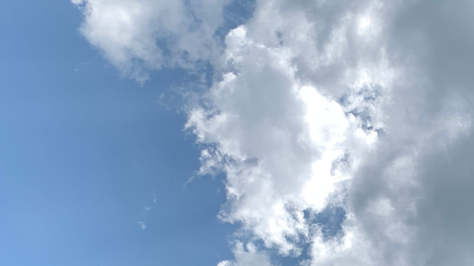 A patch of sky divided between blue sky on the left and gray-and-white cloud on the right, with a ovalish sub-cloud, vertical on the long axis, slightly separating from the main cloud and showing off a blinding white right-hand edge.  