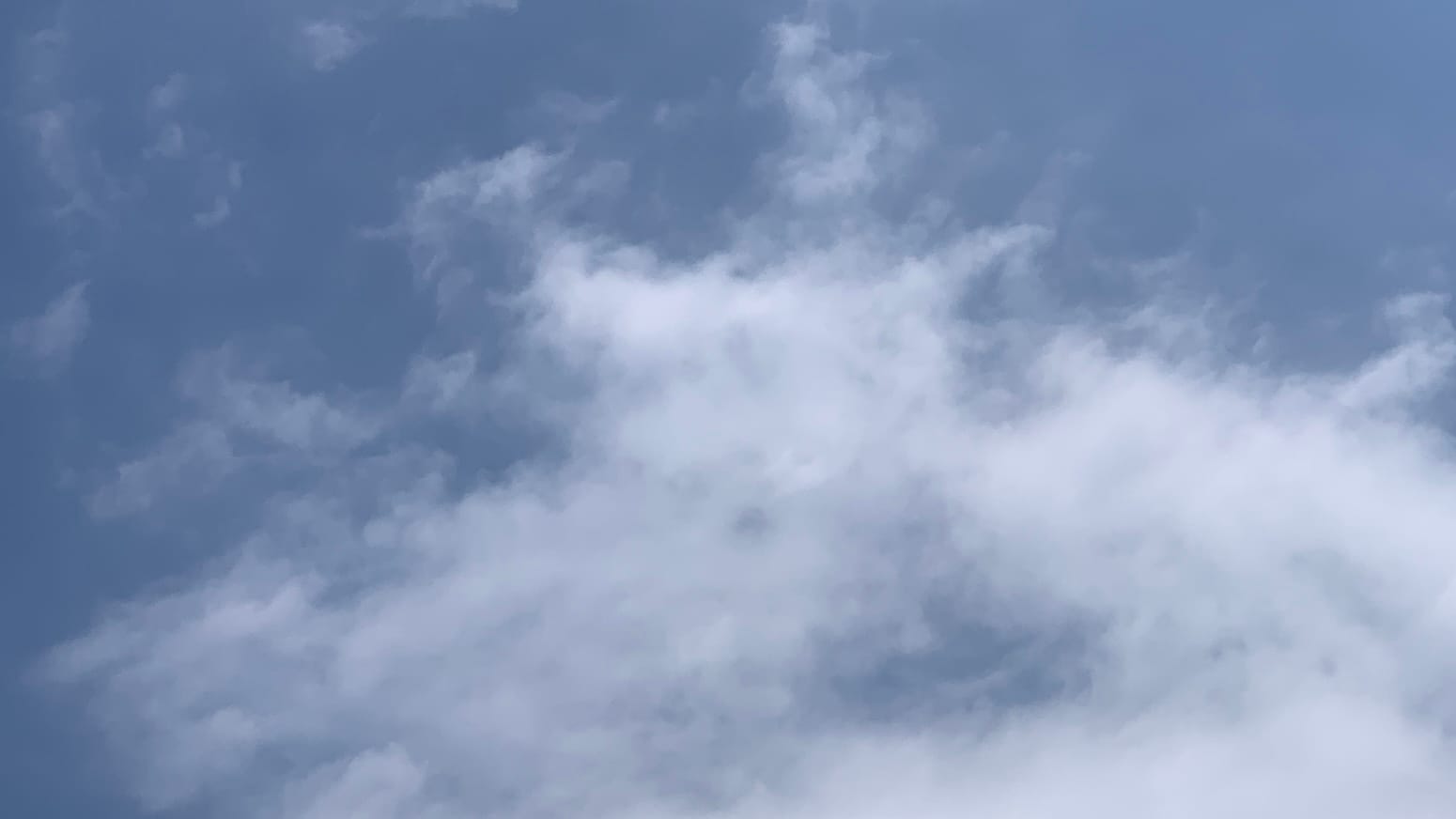 A patch of sky with loose-knit white clouds reaching up from the bottom of the flame to extend wisps and tendrils into the blue at the top. 