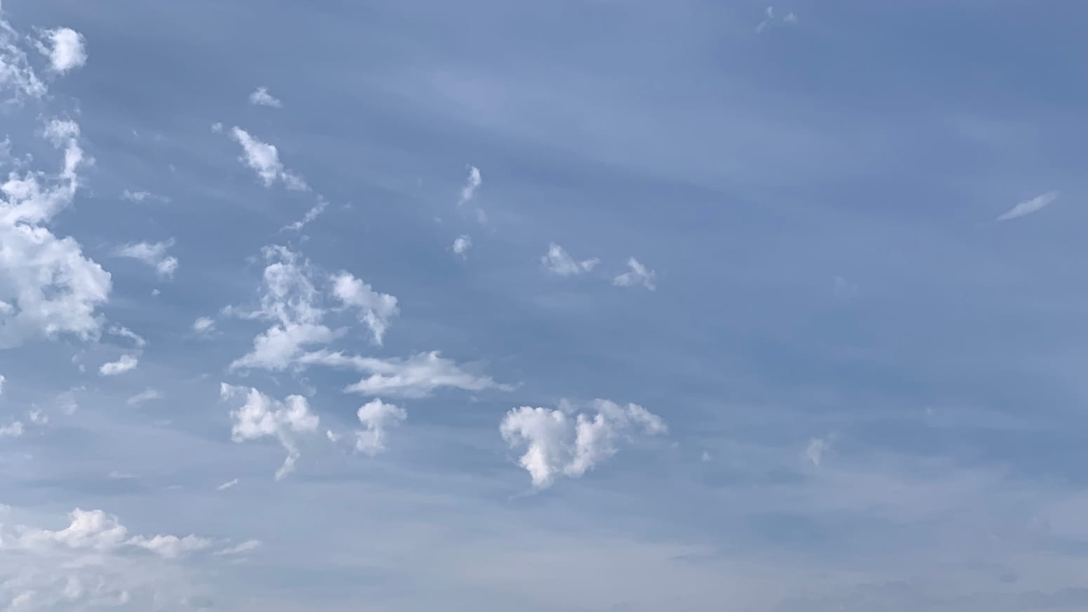 A sky streaked with translucent white on blue, underneath which a procession of little scraps of lower clouds, some of them vaguely wedge-shaped, is entering from the left side of the frame in a sort of triangular formation. A single little almost oval outrider cloud, tipped at an angle, approaches the right side of the frame. 