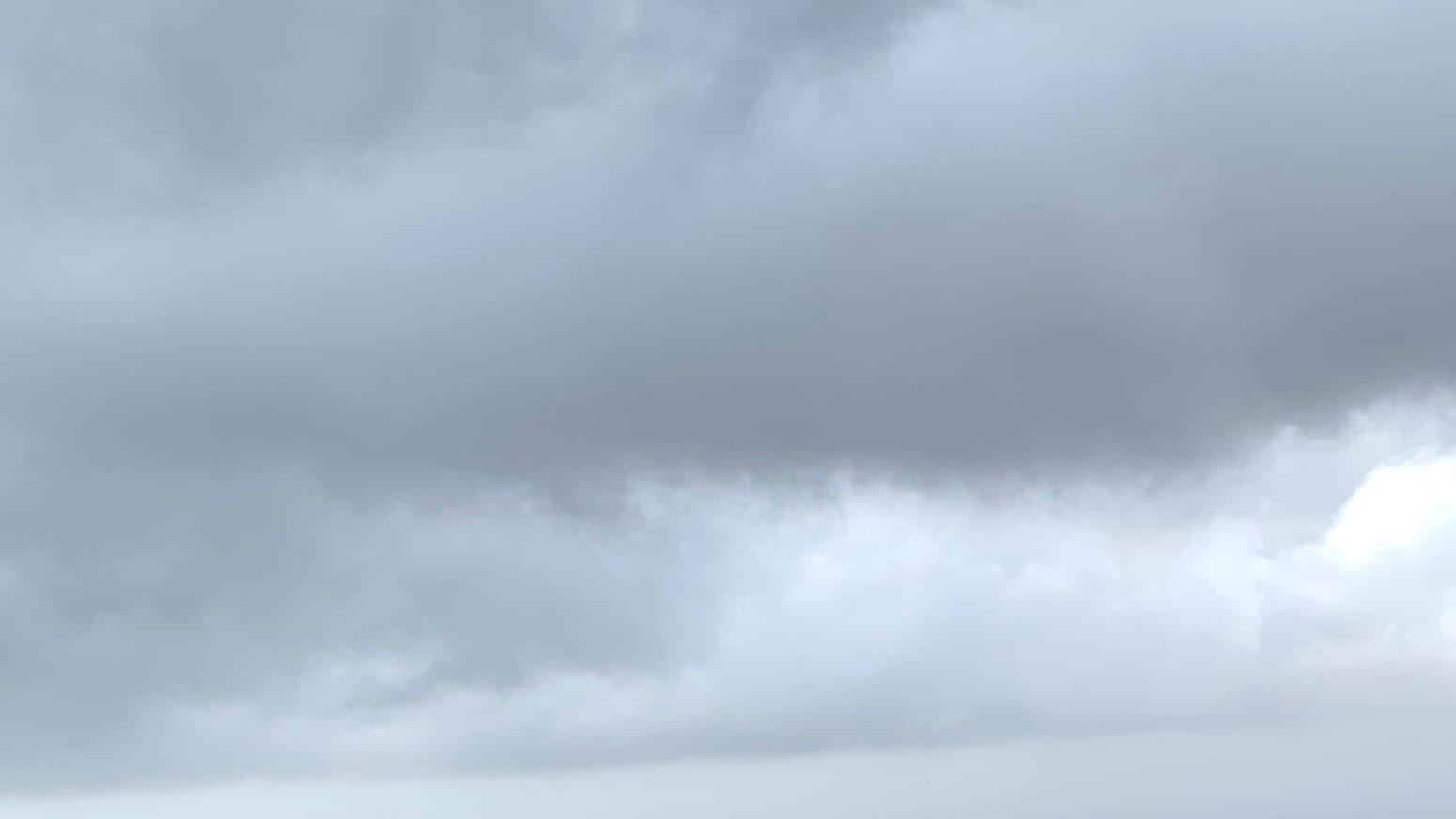 A sky of dark gray clouds filling the top half or so of the frame, with irregular lighter gray clouds below, and a sharp line separating that from an intermediate sort of gray at the bottom of the frame. 