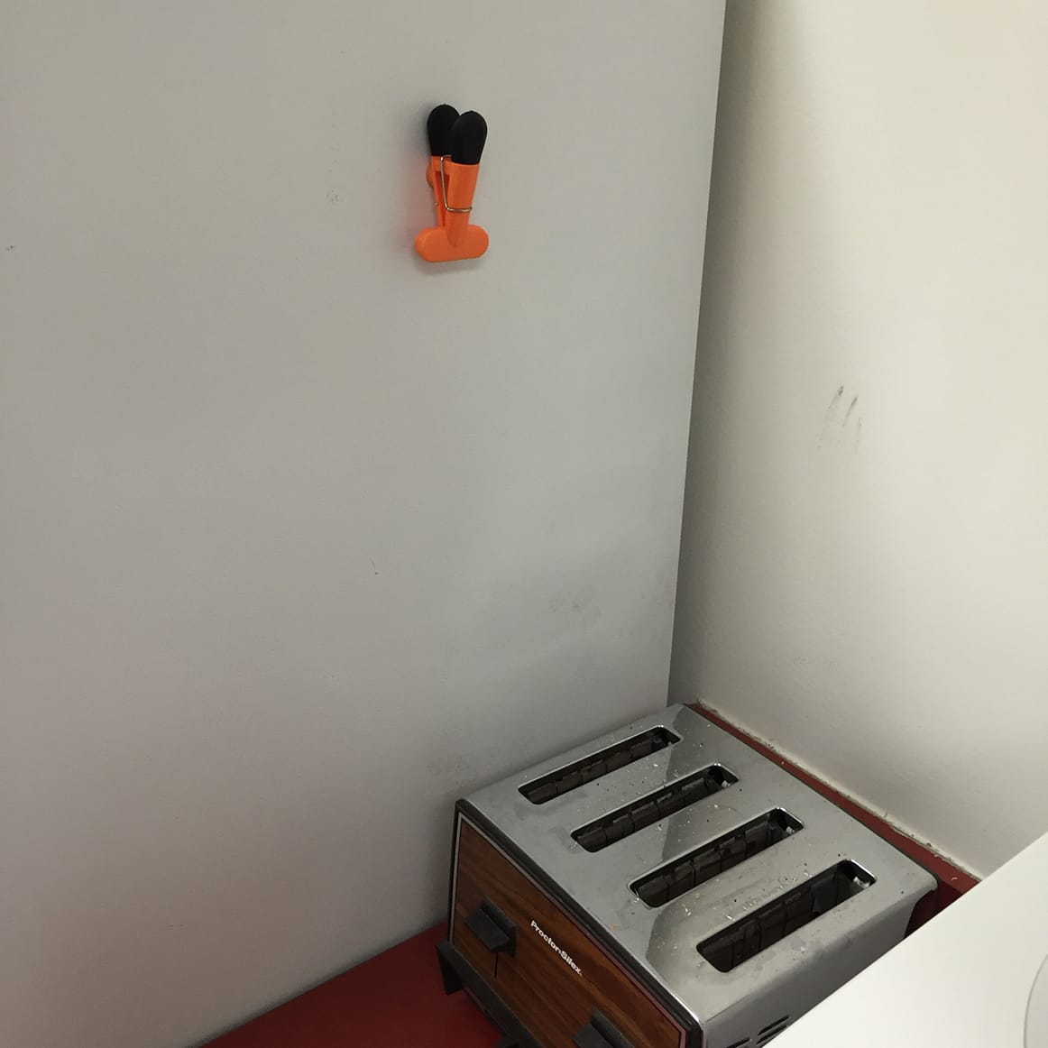 The side of the office fridge with a plastic magnetic note clip about 18 inches above a functioning four-slot toaster.