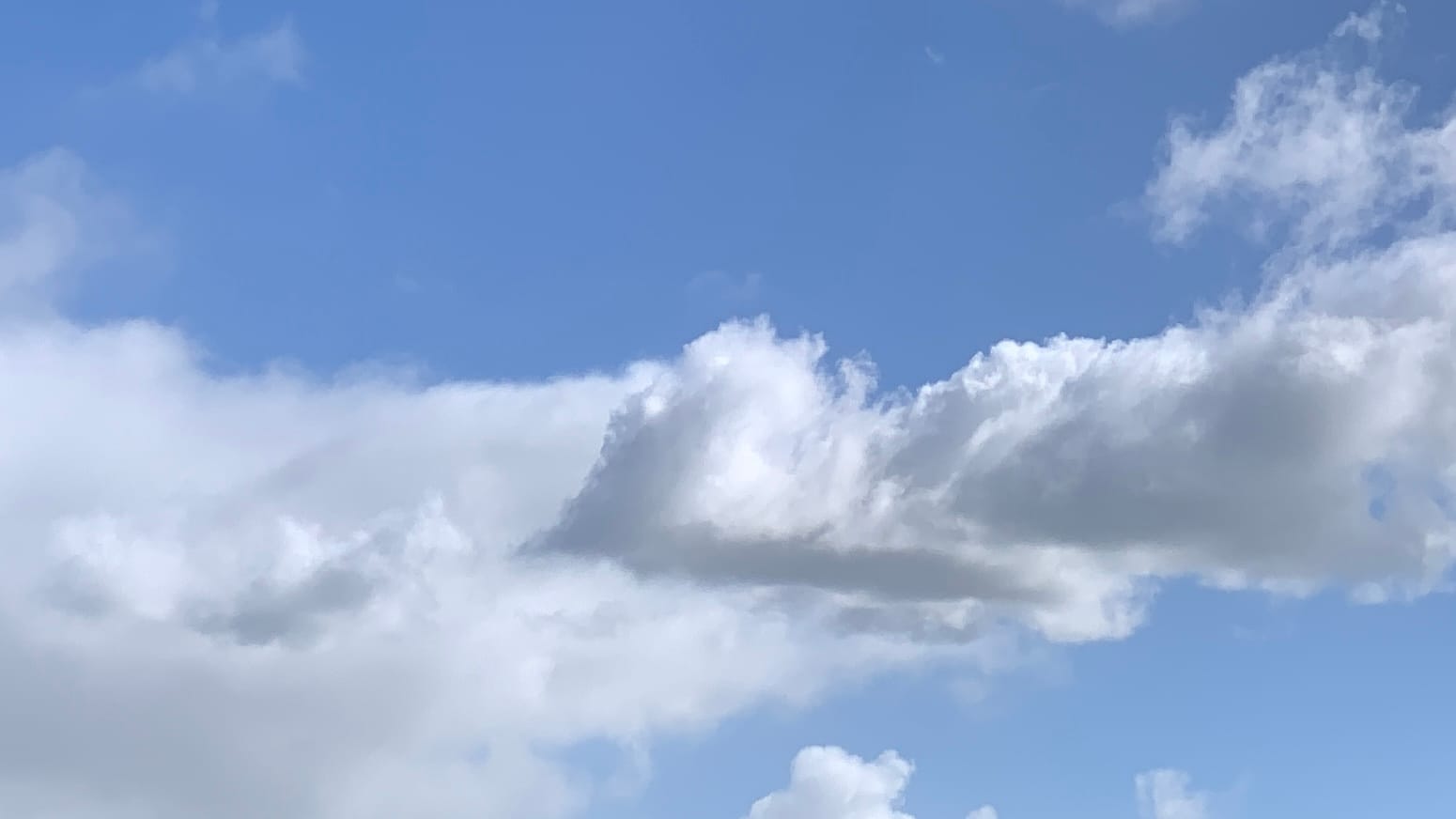 A patch of blue sky with white clouds, shaded with gray, running across the middle of the frame and reaching down into the bottom left corner. The closer clouds are almost angular; and the ones behind them are more shapeless. 