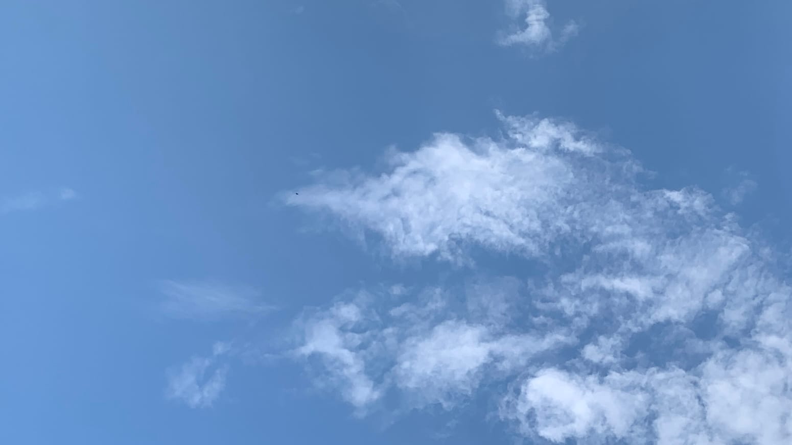 Blue sky with a wave- or shark-fin-shaped arrangement of loose-knit wispy clouds rising from the bottom right corner of the frame and curving toward the middle.