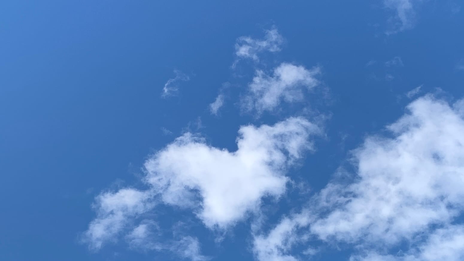 Blue sky with a loose-knit white cloud in the center and more loose white clouds in the bottom right corner. 