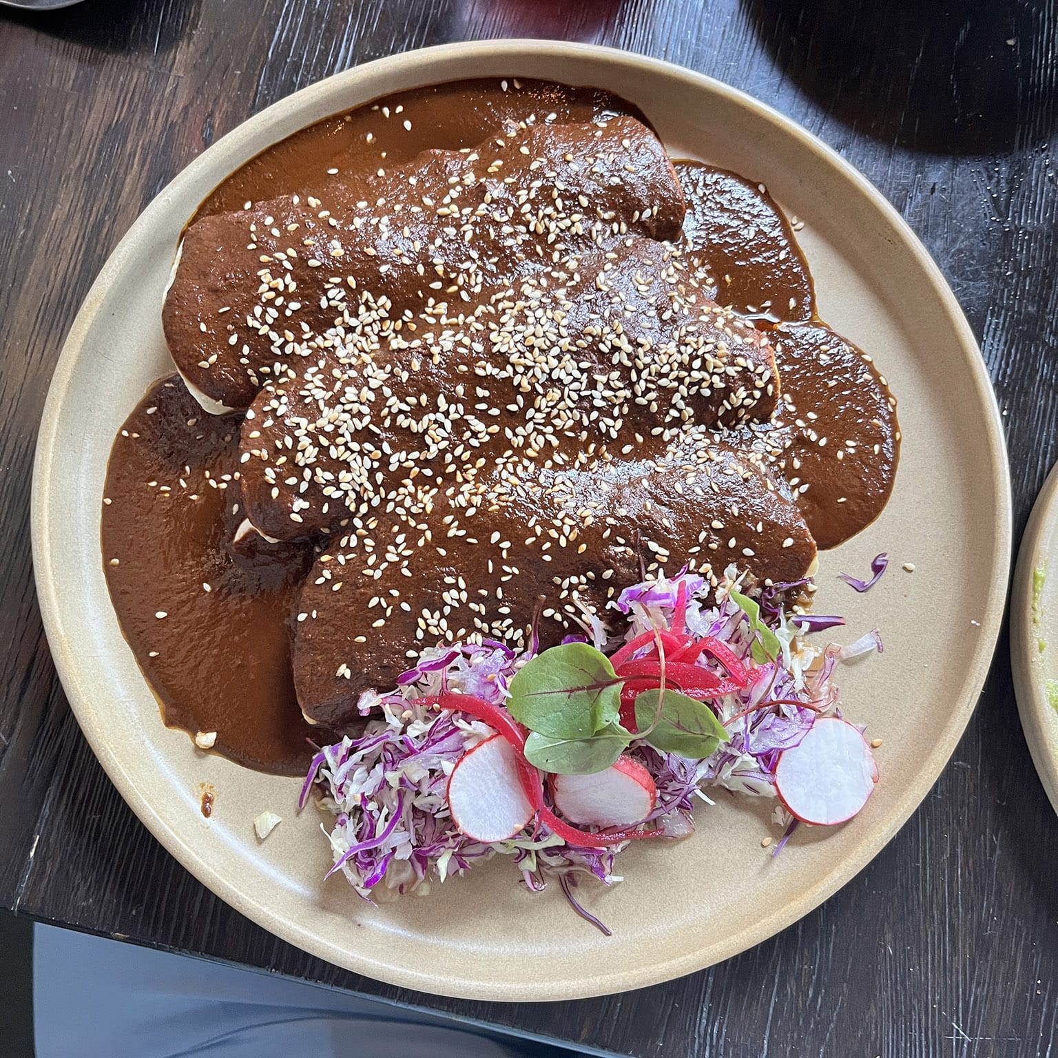 Beef Enchiladas with Mole corn tortillas filled with prime beef chuck barbacoa, with Oaxacan mole topped with cabbage, sour cream, queso fresco, pickled onions, and sesame seeds