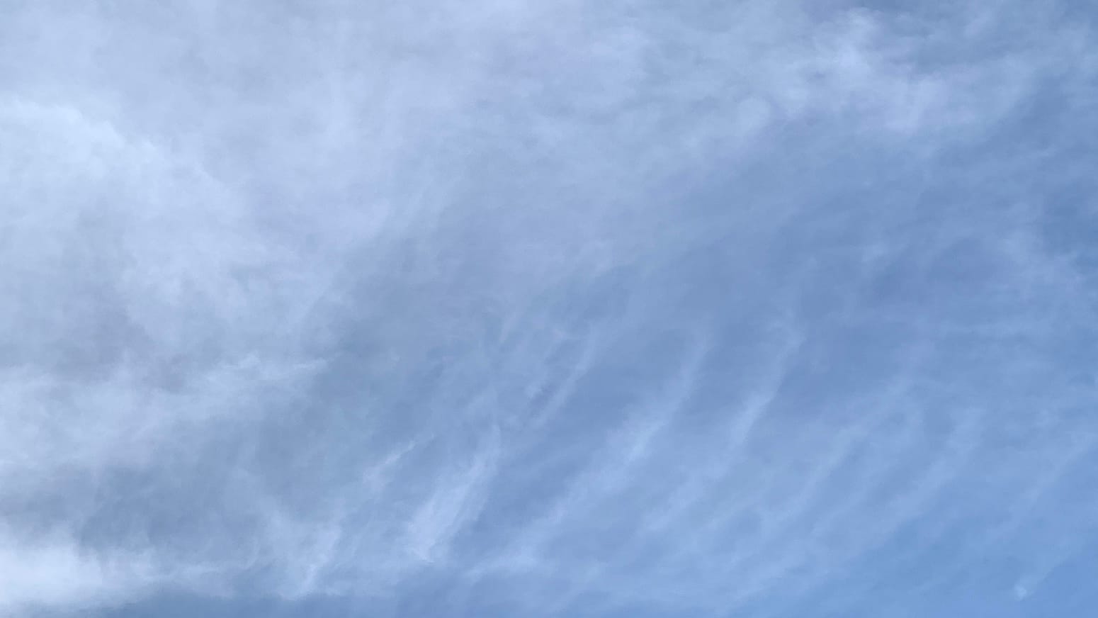A patch of blue sky with translucent white clouds on it, a mostly solid sheet toward the upper left giving way to a row of curving lines in the lower right.