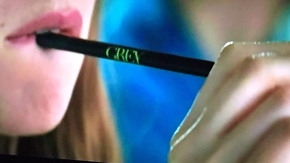 The star of the movie putting a pencil with GREY on it into her mouth.