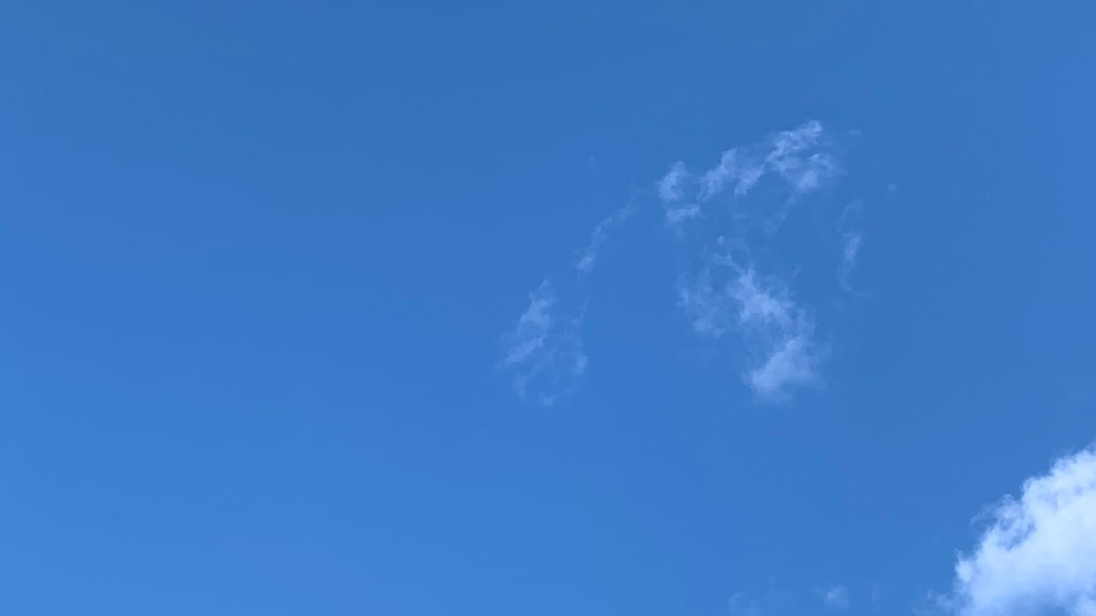 A patch of blue sky with a tenuous cloud-skeleton of fractus floating in the center-right and a denser bit of white cloud down in the bottom right corner. 
