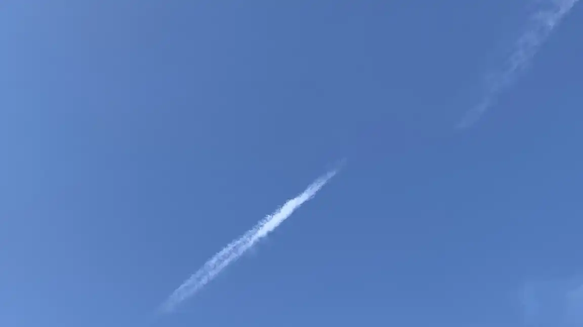 A patch of bright blue sky with a truncated, bright-tipped contrail angling from lower left toward upper right, and a similarly aligned but separate bit of contrail dissolving in the upper right corner.
