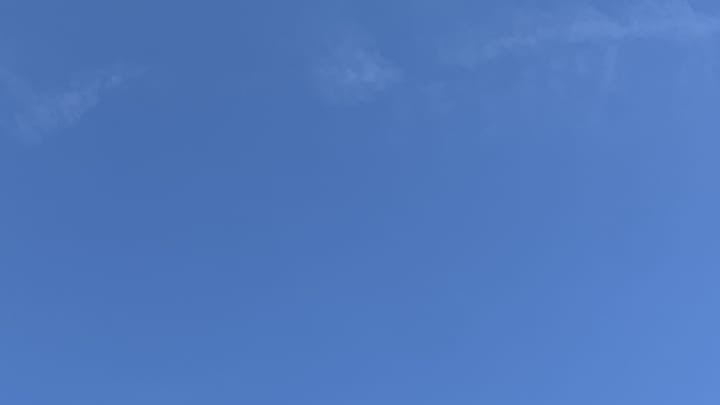 A patch of blue sky with the faint, dissolving traces of a contrail spread across the top of the frame. 