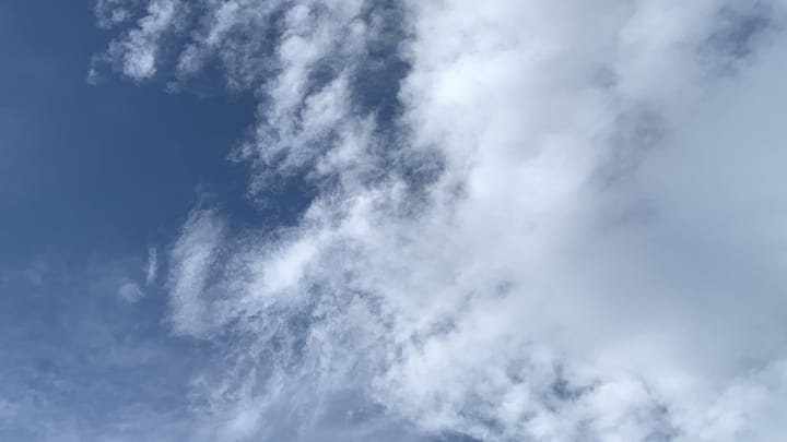A complicated patch of sky with a section dark blue sky along the left side, covered in high filmy clouds at bottom left, and next to that bright white thinly fleecy streaks and wisps superimposed on the blue, and next to that, from about the middle of the picture rightward, blurry white clouds superimposed on those. 