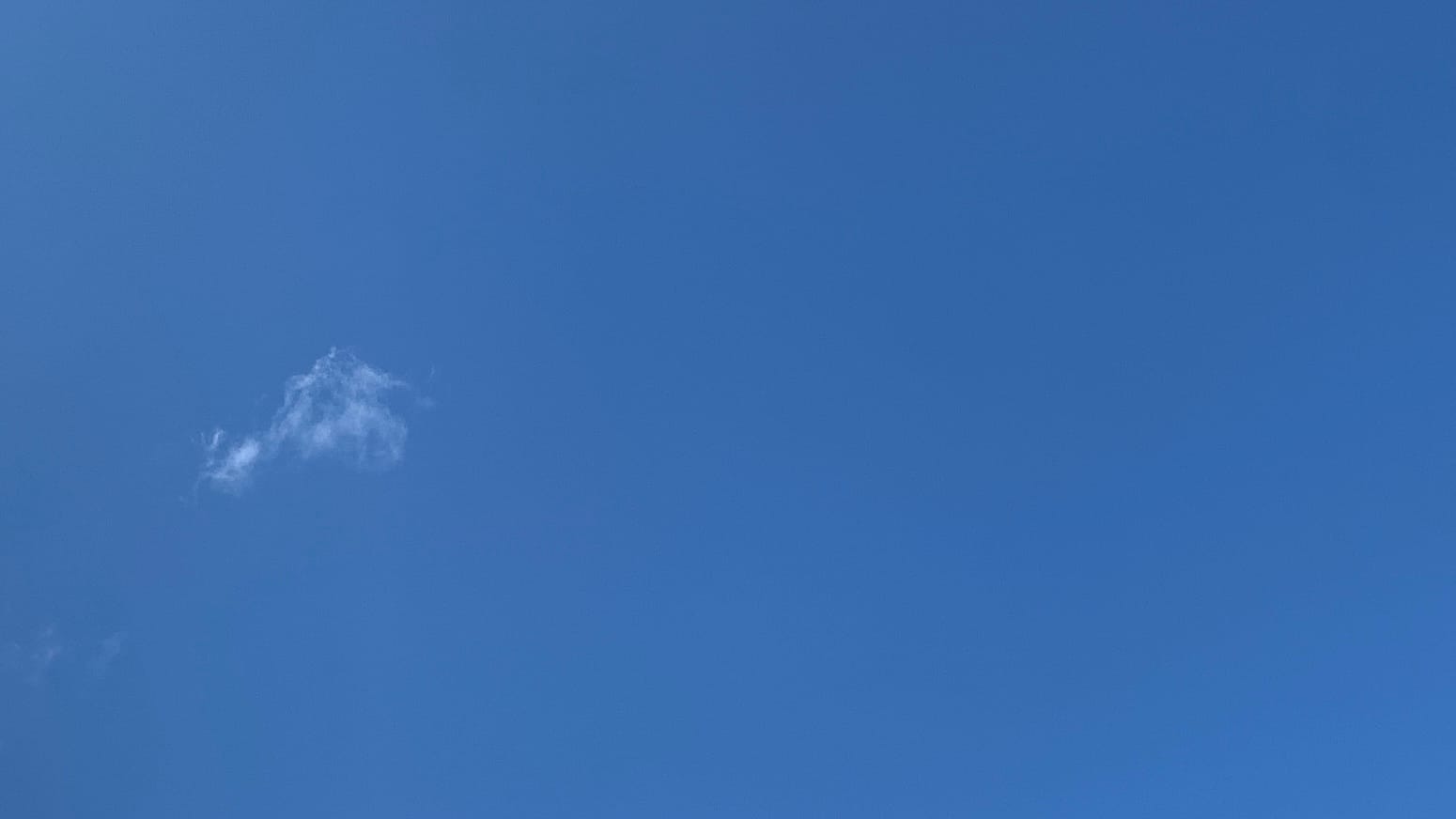 A patch of clear deep blue sky with a bit of white fractus cloud floating in the middle of the left side and some near-invisible extra shreds below and even closer to the edge. 