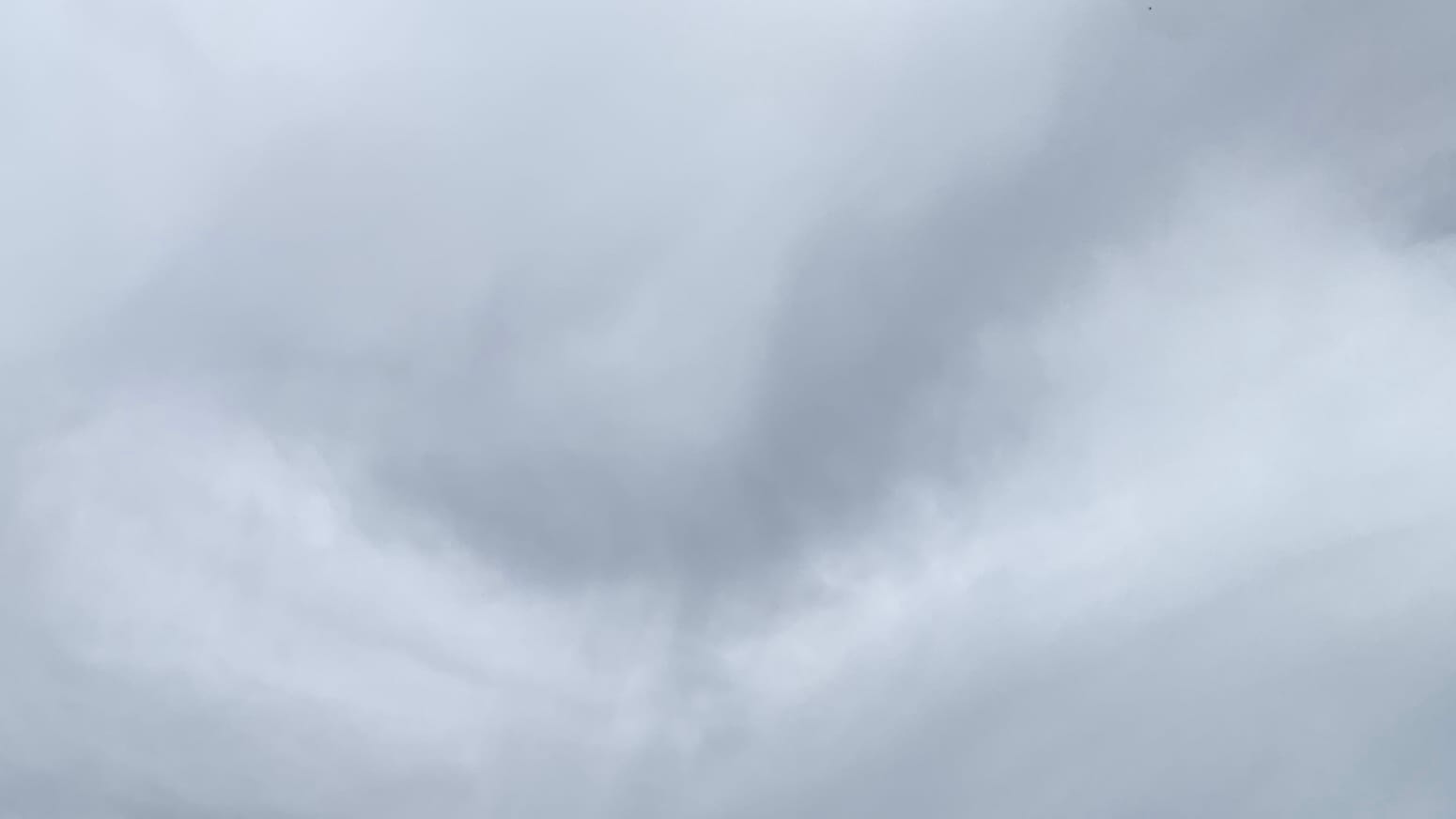 A gray cloudy sky with a lighter stretch like a flattened U running across the middle and a darker, similarly curved but more lopsided stretch nestled atop it, reaching up to the top right corner.  