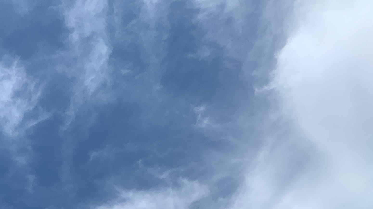 A patch of blue sky with thinned-out white scraps of cloud on it and a denser bulge of cloud pushing in from the right side of the frame.