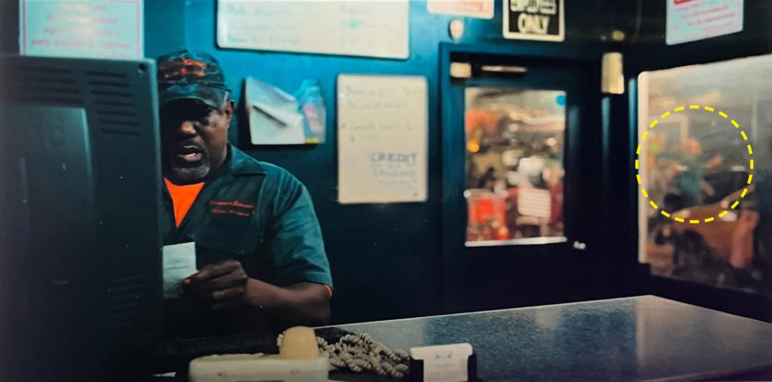 Scene at a car repair shop, and the mechanic is in the foreground, and beyond a gimy window, blurred out, you can almost make out a figure pointing at stuff.