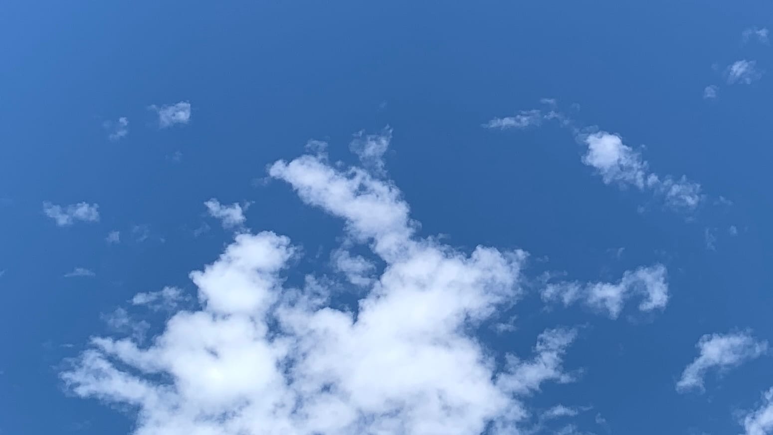 A patch of deep blue sky with a loosely assembled white cloud entering the bottom of the frame and occupying the middle bottom left. The cloud has blue fissures in it and various scraps of unincorporated cloud nearby.