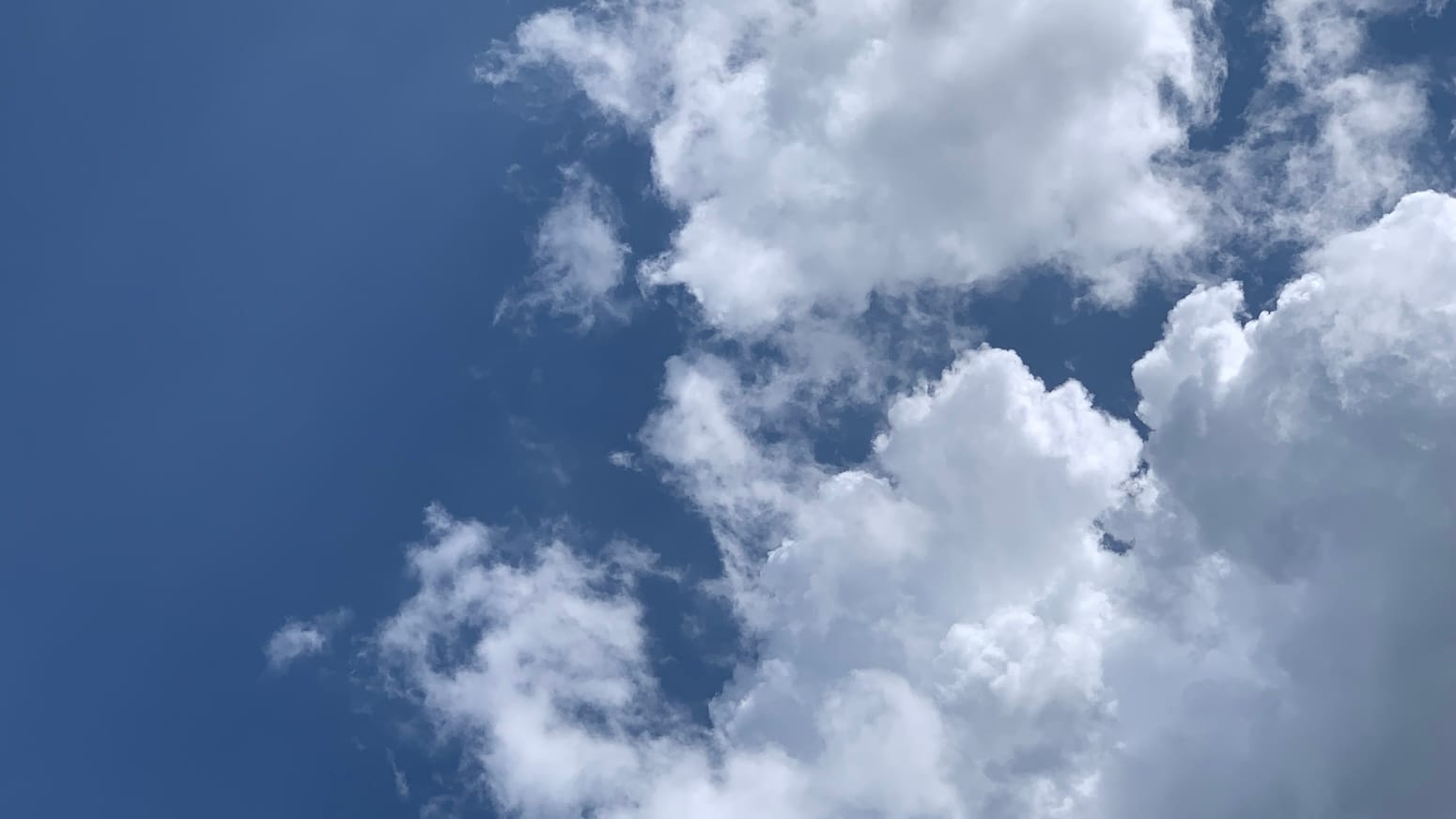 A patch of deep blue sky with large, brilliantly lit cumulus filling the bottom right corner and top middle of the frame, with a deep blue rift between them. 